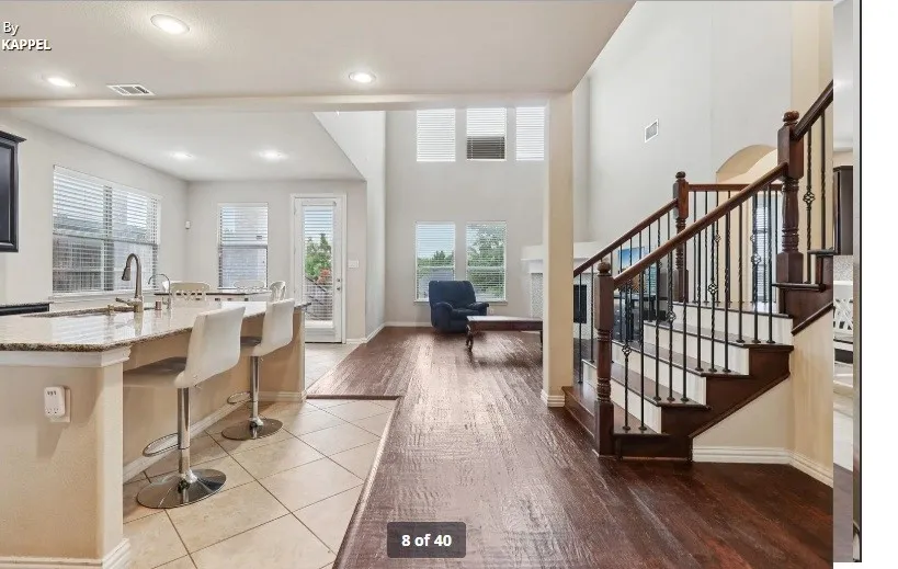 Two-story interior with wood-finish flooring, a kitchen island with a stone countertop, a white tile floor, and a staircase featuring wood handrails and wrought iron balusters