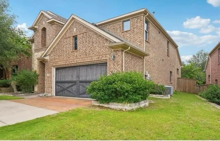 Brick exterior with stone accents, an attached garage featuring a dark wood-finish door, and a manicured lawn