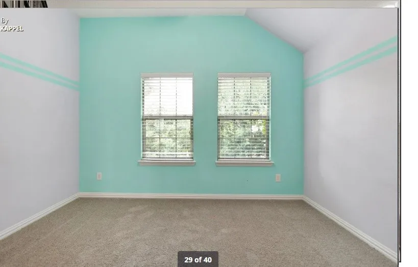 Twin windows with blinds, pitched ceiling, light-colored carpeting, and painted walls