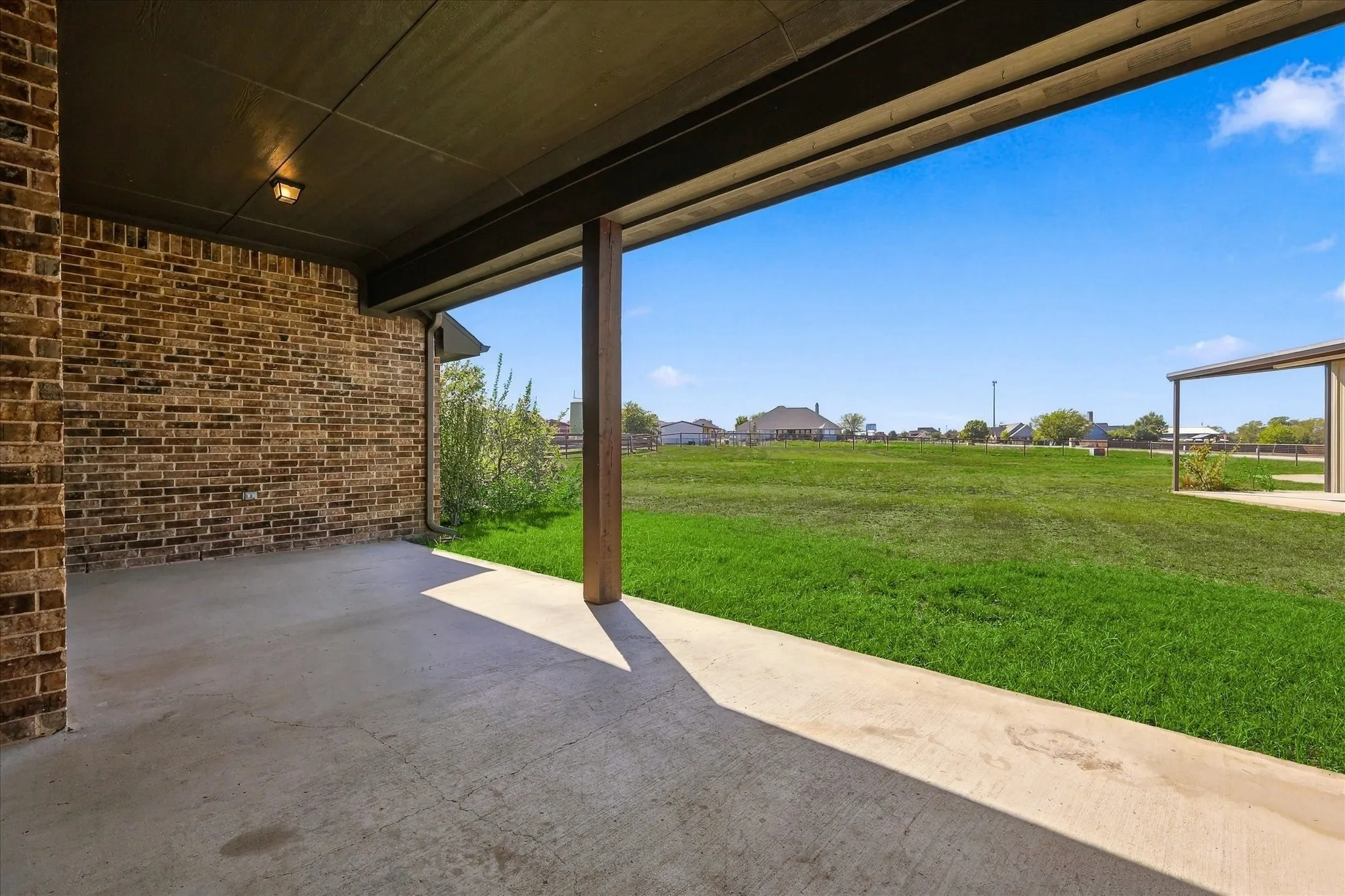 Covered patio with a concrete surface, brick exterior wall, and wood-finish support column
