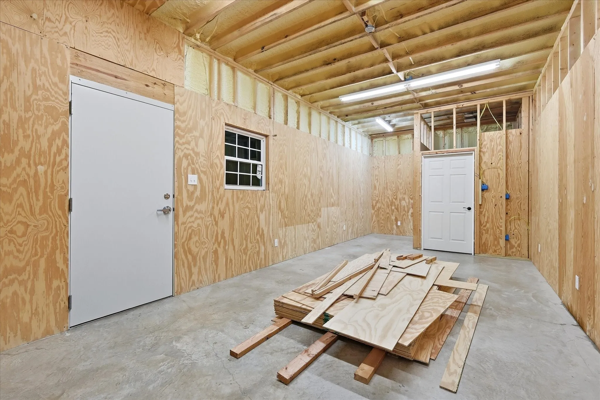 Concrete flooring, exposed wood framing, wood-panel walls, white panel doors, and a white grid window