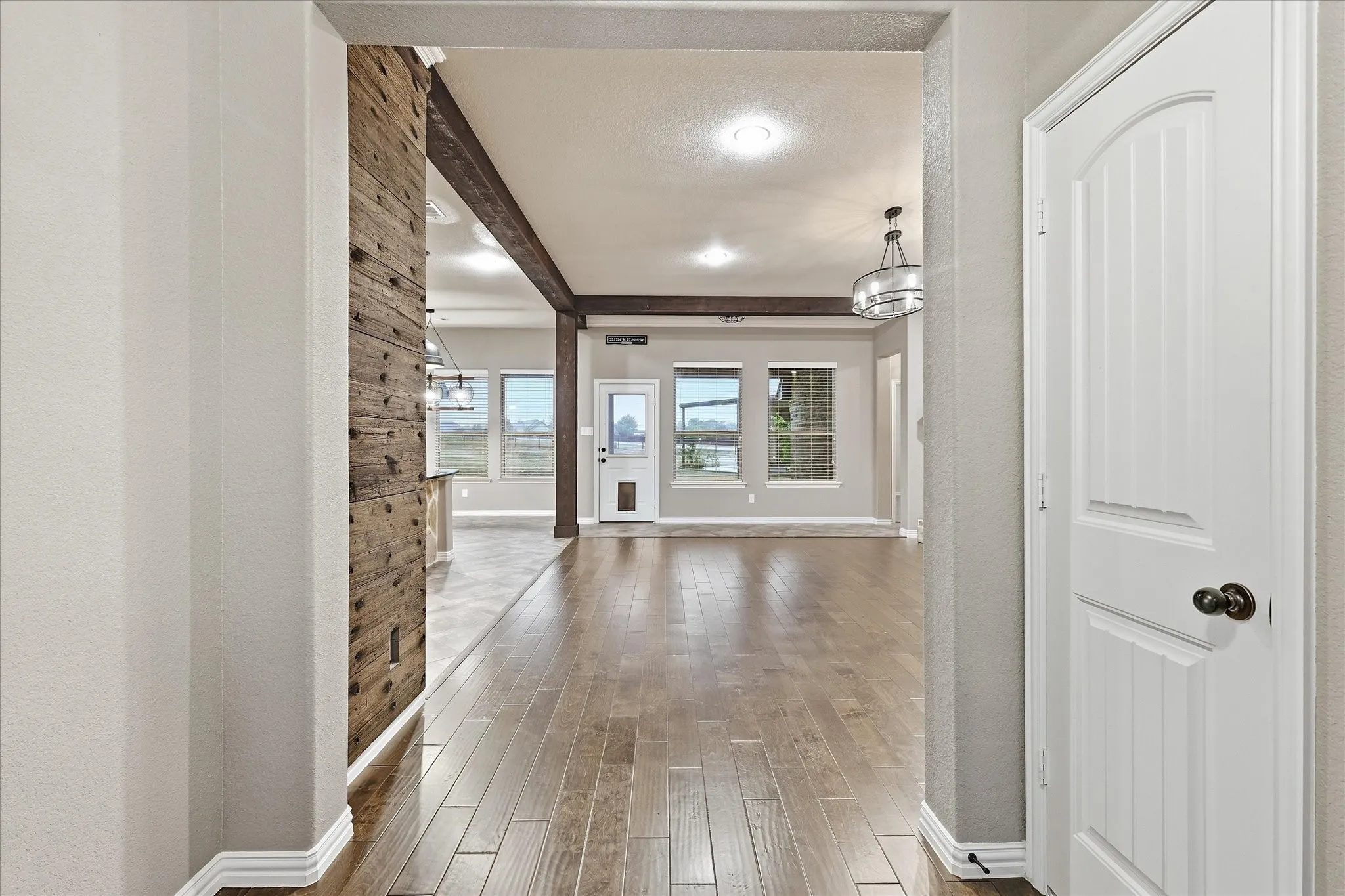 Expansive interior featuring wood-finish flooring, a wood-paneled accent wall, exposed ceiling beams, and recessed lighting