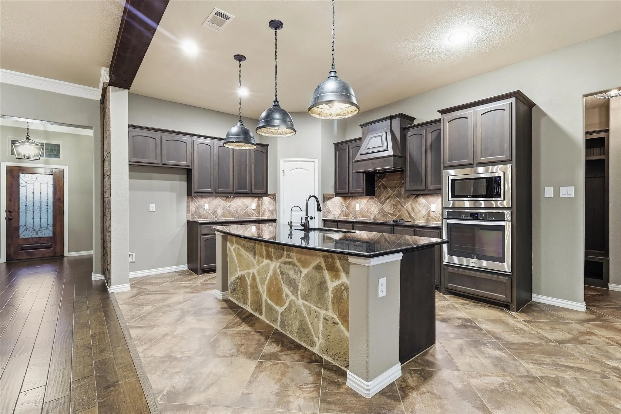 Kitchen featuring dark wood-finish cabinetry, built-in stainless steel appliances, a stone-faced island with a black countertop, and pendant lighting