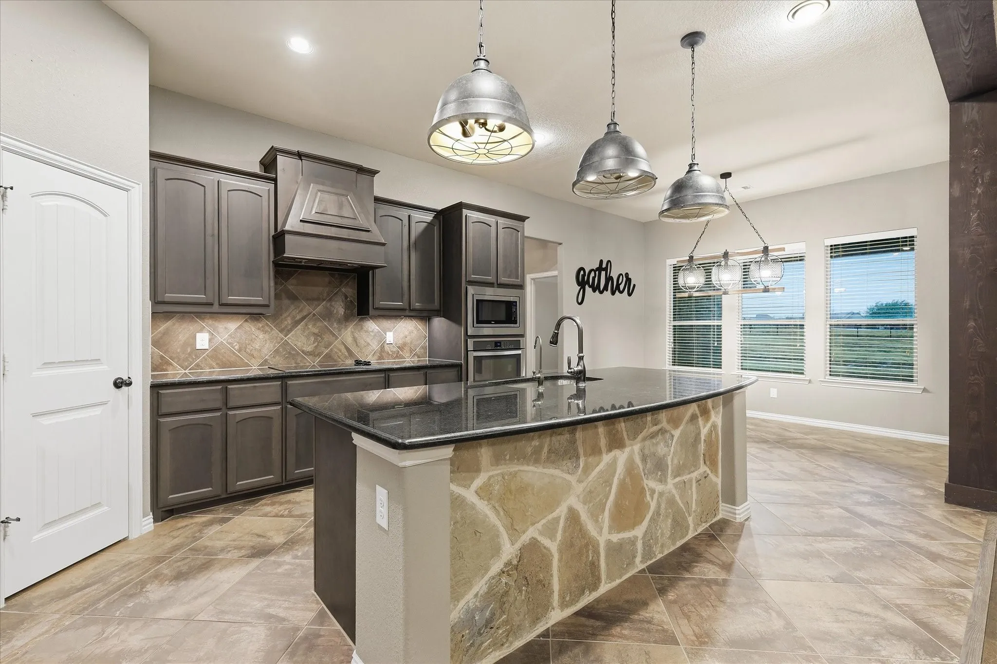Kitchen featuring dark wood-finish cabinetry, built-in stainless steel appliances, stone tile backsplash, a center island with a stone facade, and overhead pendant lighting