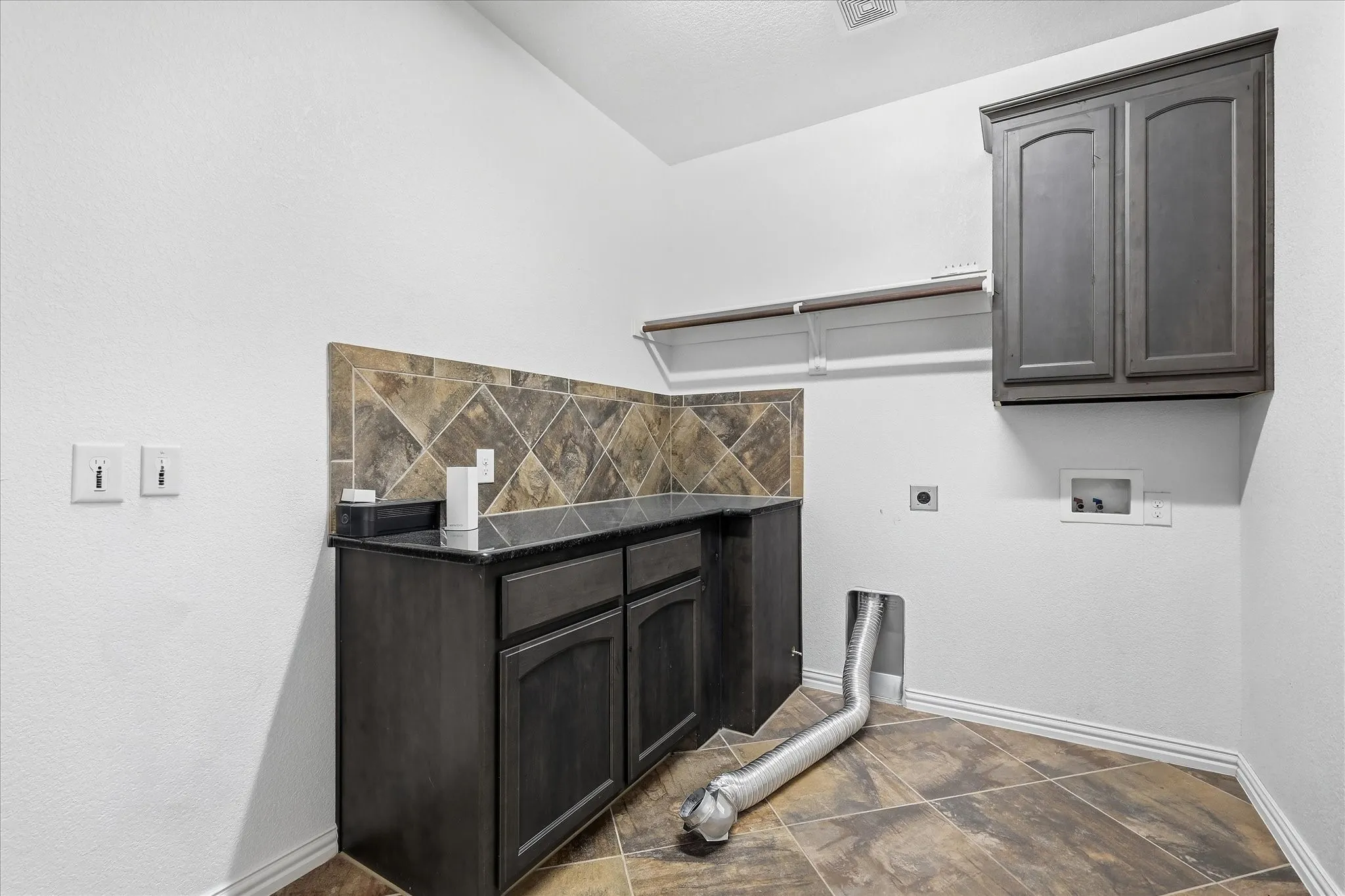 Cabinetry with dark finish, tile backsplash, dark countertop, and tiled flooring