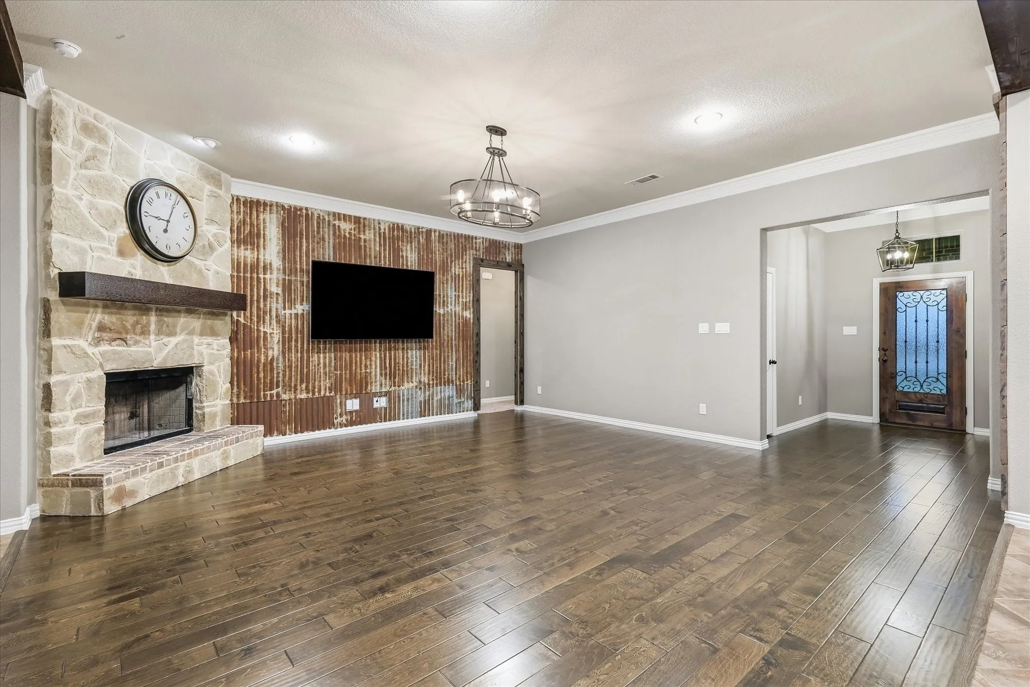 Expansive living area with wood-finish flooring, a stone-clad fireplace, and a corrugated metal accent wall