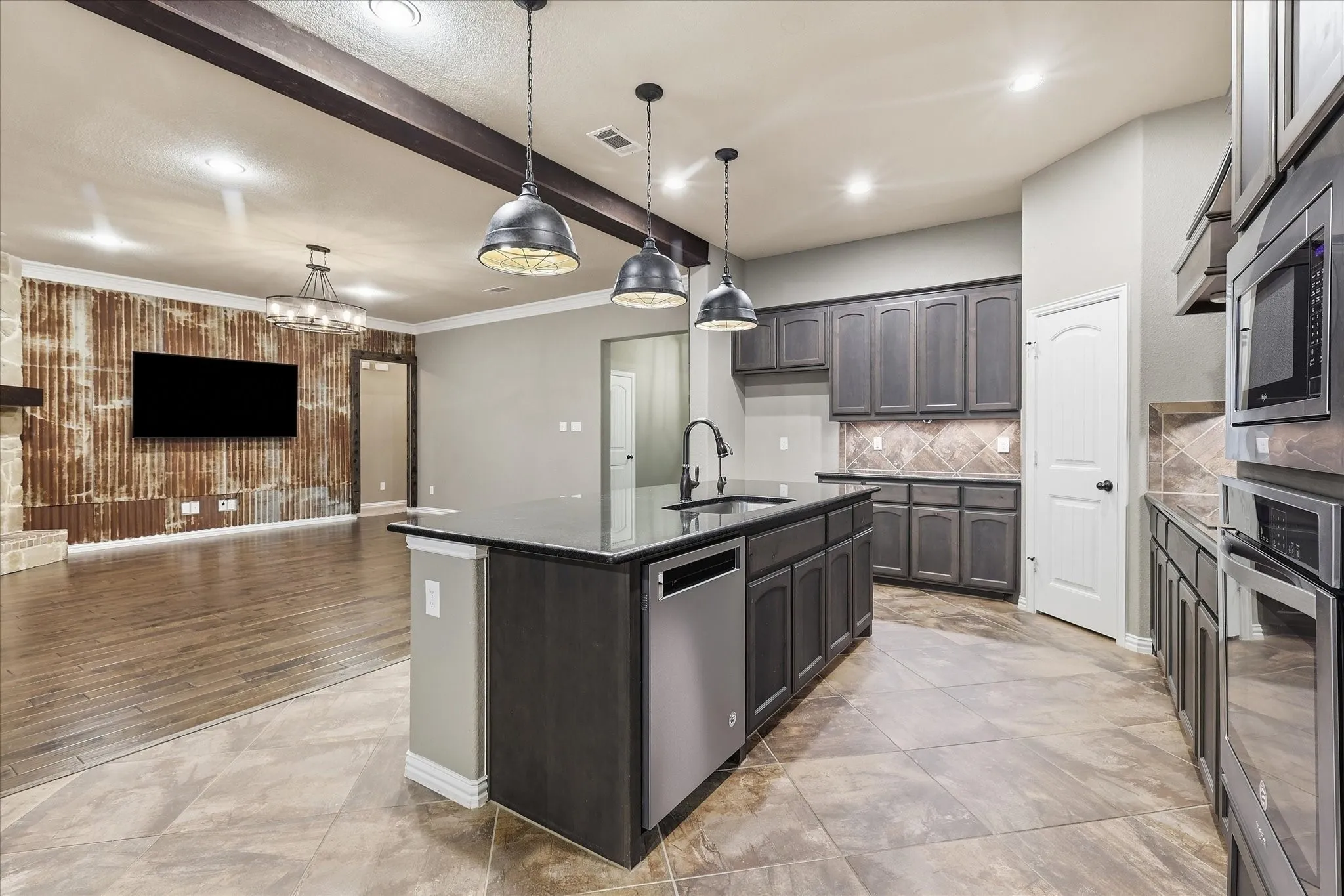 Kitchen featuring a central island with a built-in dishwasher, dark cabinetry, dark countertops, and integrated wall ovens