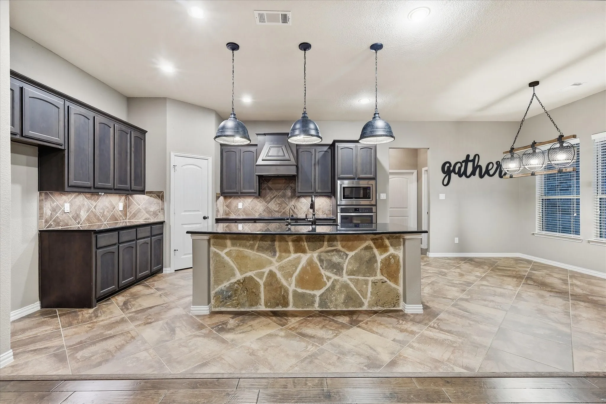 Spacious kitchen with a stone-clad island, pendant lighting, built-in appliances, and tile flooring