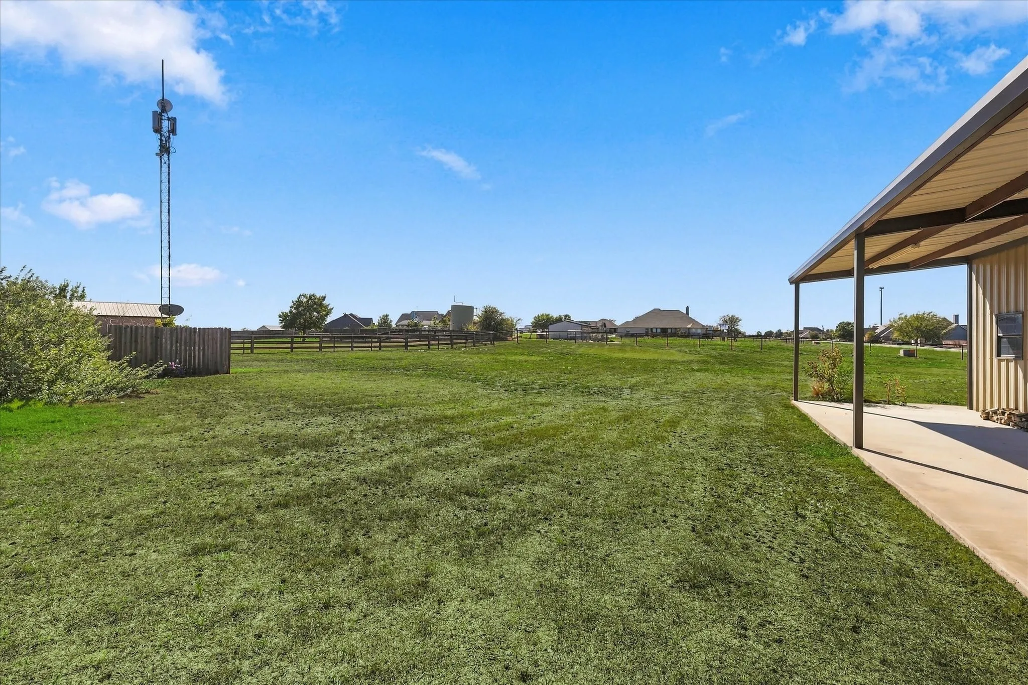 Expansive grassy area with a partial privacy fence and an open-sided covered structure featuring a concrete pad