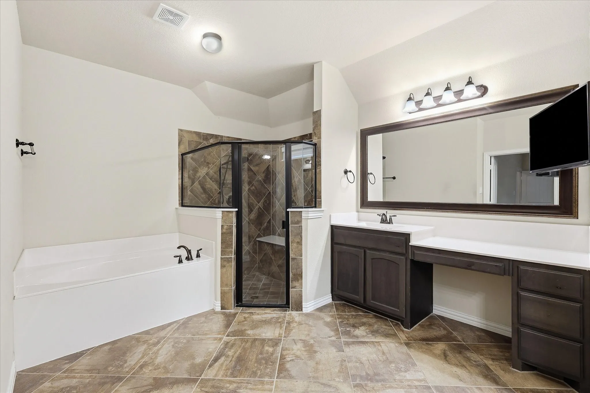 Tile flooring, built-in soaking tub, walk-in shower with bench, dark wood-finish vanity with countertop, and large framed mirror