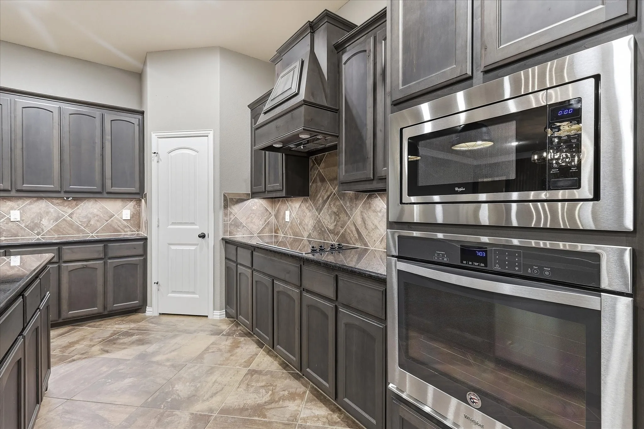 Built-in stainless steel microwave and oven, dark cabinetry, recessed lighting, and tile flooring