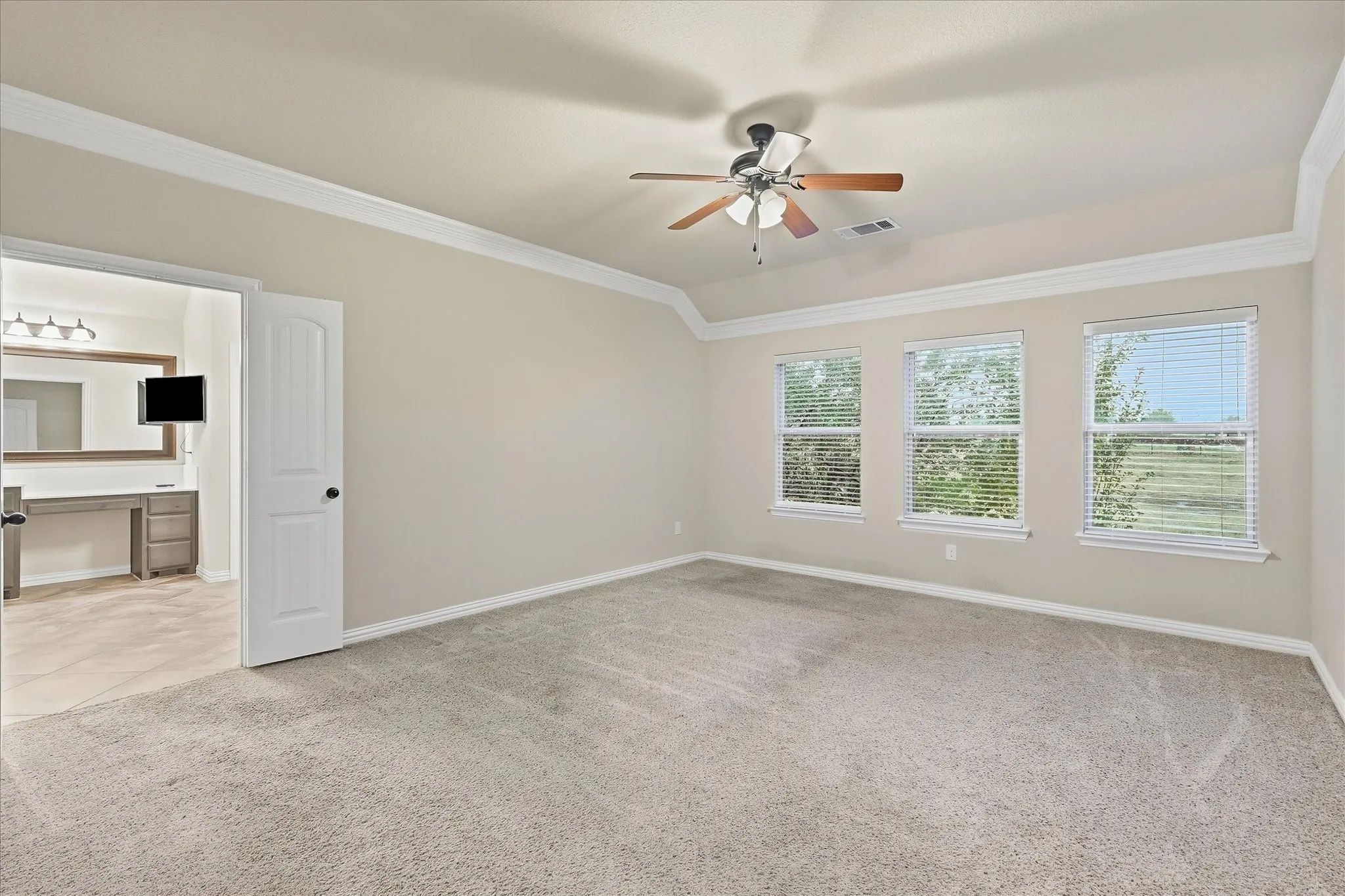 Spacious room with carpet flooring, three large windows, a ceiling fan with integrated lighting, and crown molding