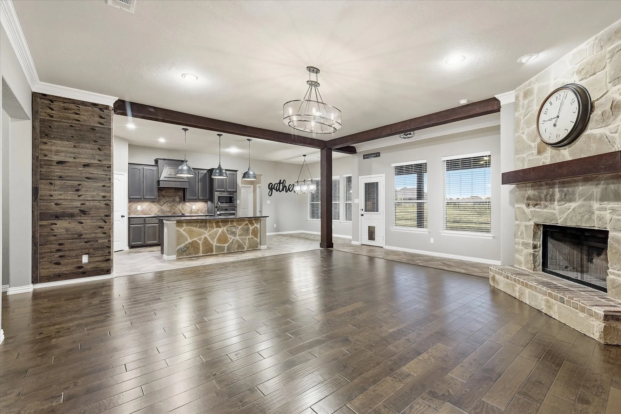 Wood-finish flooring, stone fireplace with a wood mantle, exposed wood beams, multiple windows, and a built-in kitchen island with stone detailing