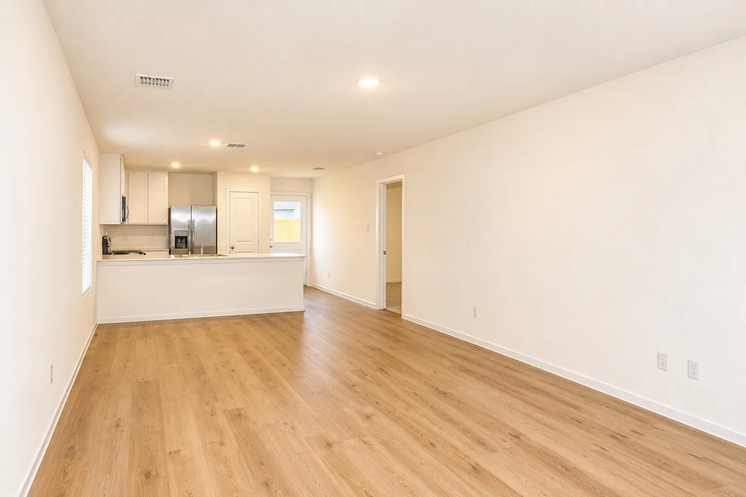 Open-concept living space with wood-finish flooring, recessed lighting, and a kitchen featuring white cabinetry, a stainless steel refrigerator, and a breakfast bar
