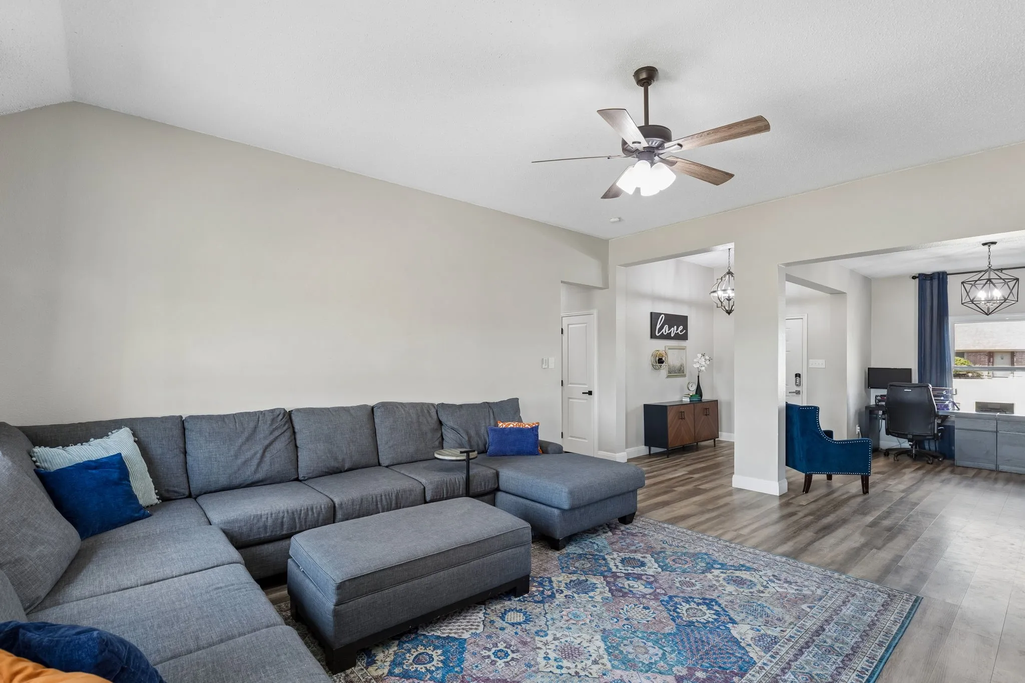 Vaulted ceiling with a ceiling fan, light-toned walls, wood-finish flooring, and open archways