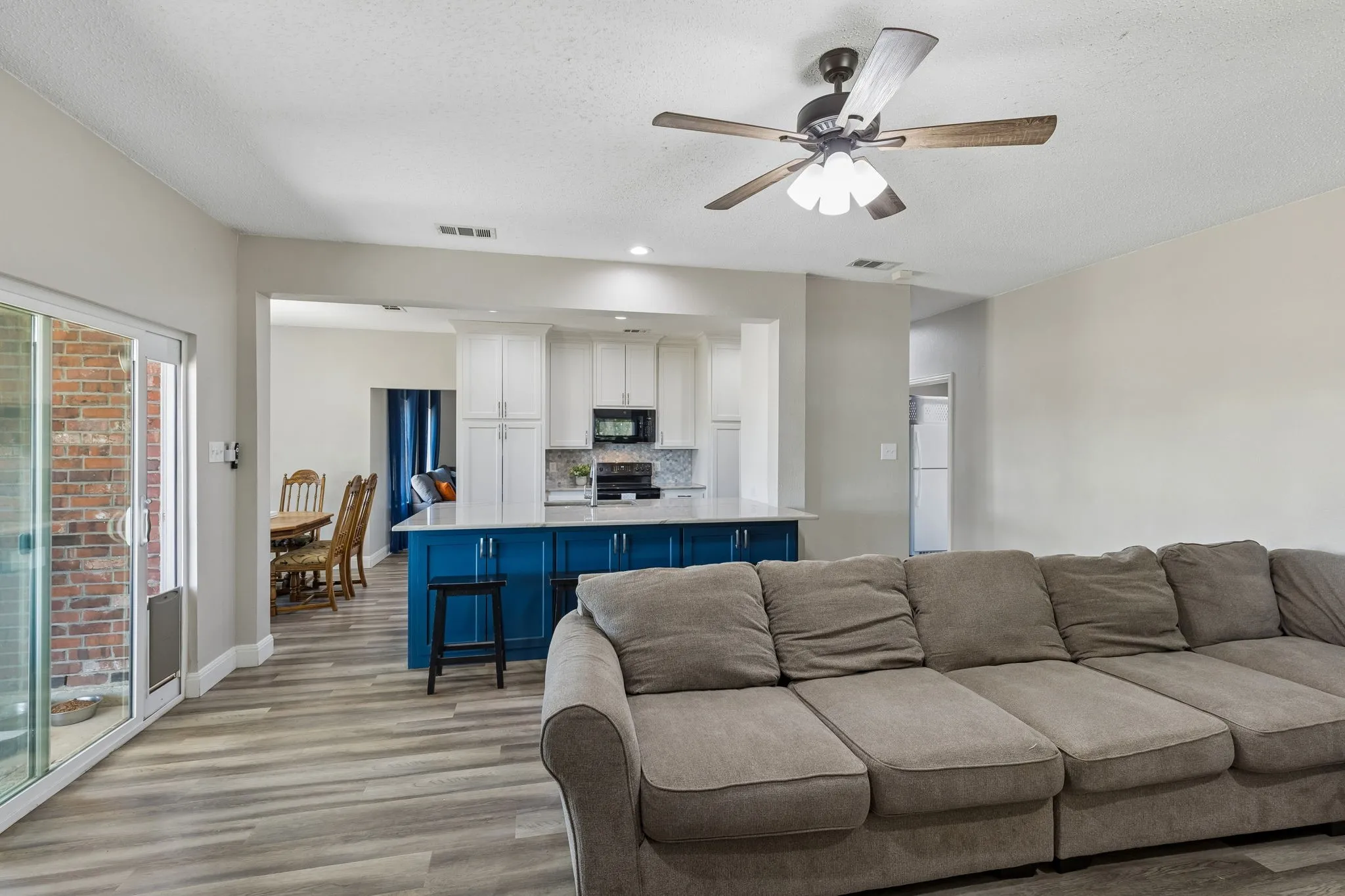 Open-concept living area with wood-finish flooring, ceiling fan, and sliding glass door