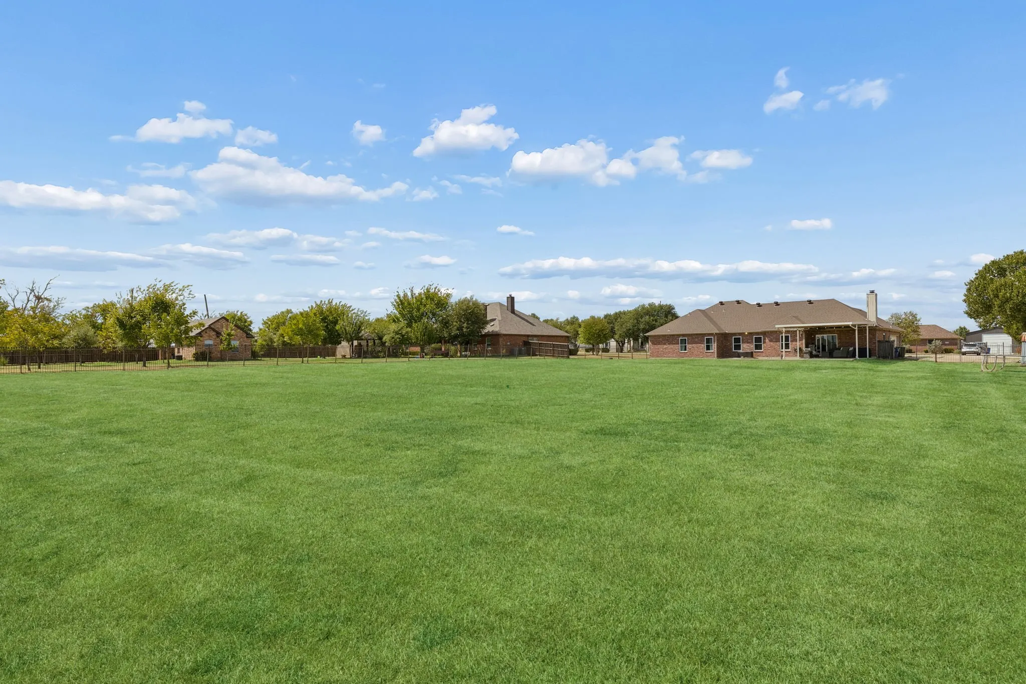Expansive lawn with mature trees and a fenced perimeter