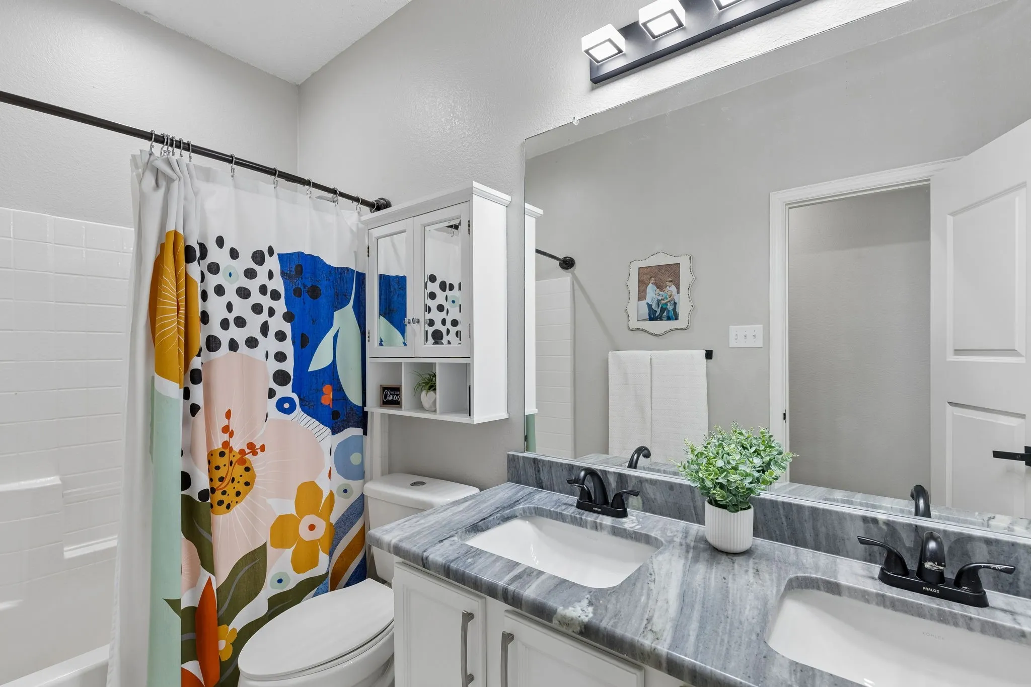 Dual vanity with gray stone countertop, white shaker cabinetry, and black fixtures