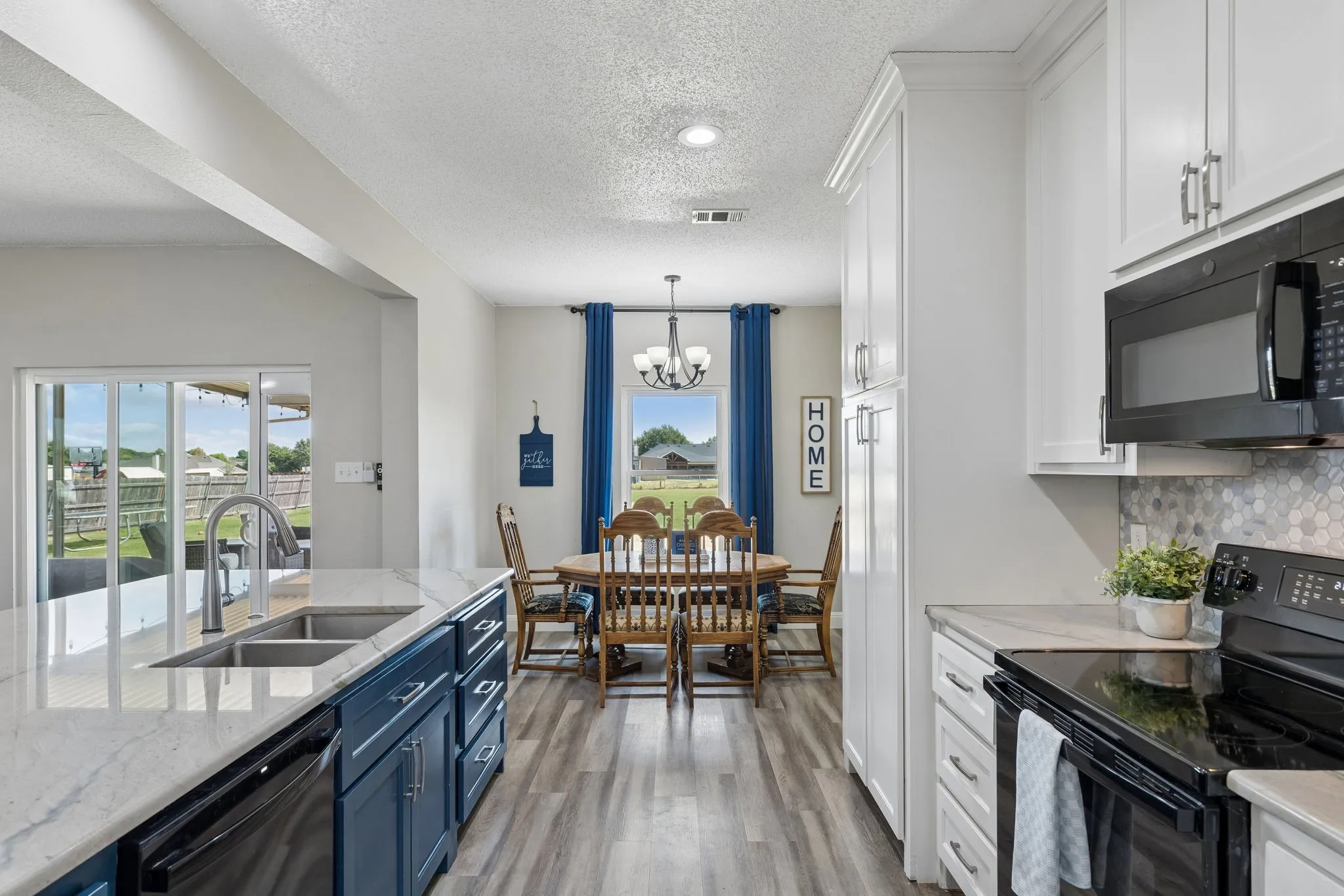 Kitchen featuring white upper cabinetry, blue lower cabinetry, stainless steel sink, black built-in appliances, and light-toned countertops