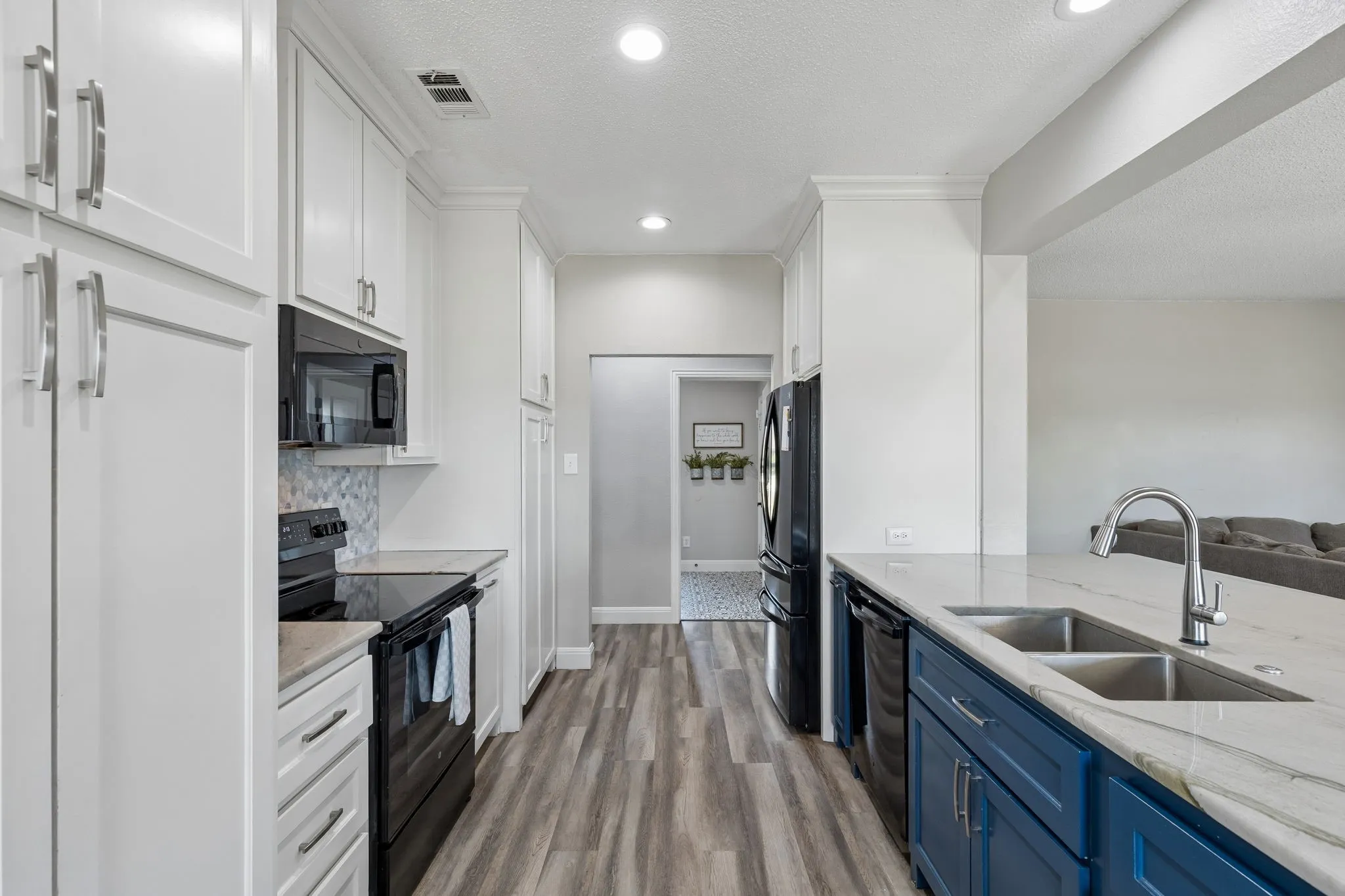 Galley kitchen with wood-finish flooring, white cabinetry, dark blue base cabinets, a double basin sink, and recessed lighting