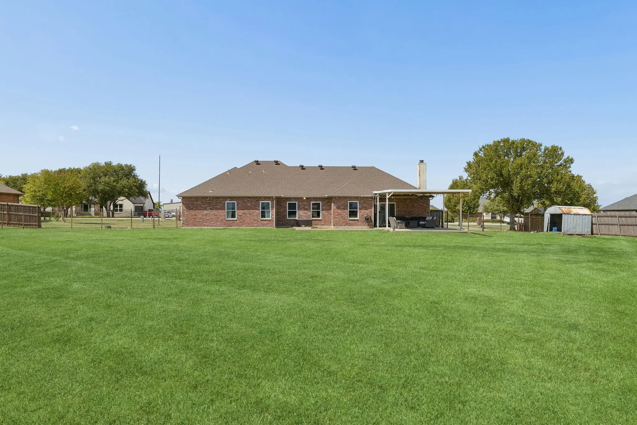 Expansive lawn with a brick exterior, covered patio, and a storage shed