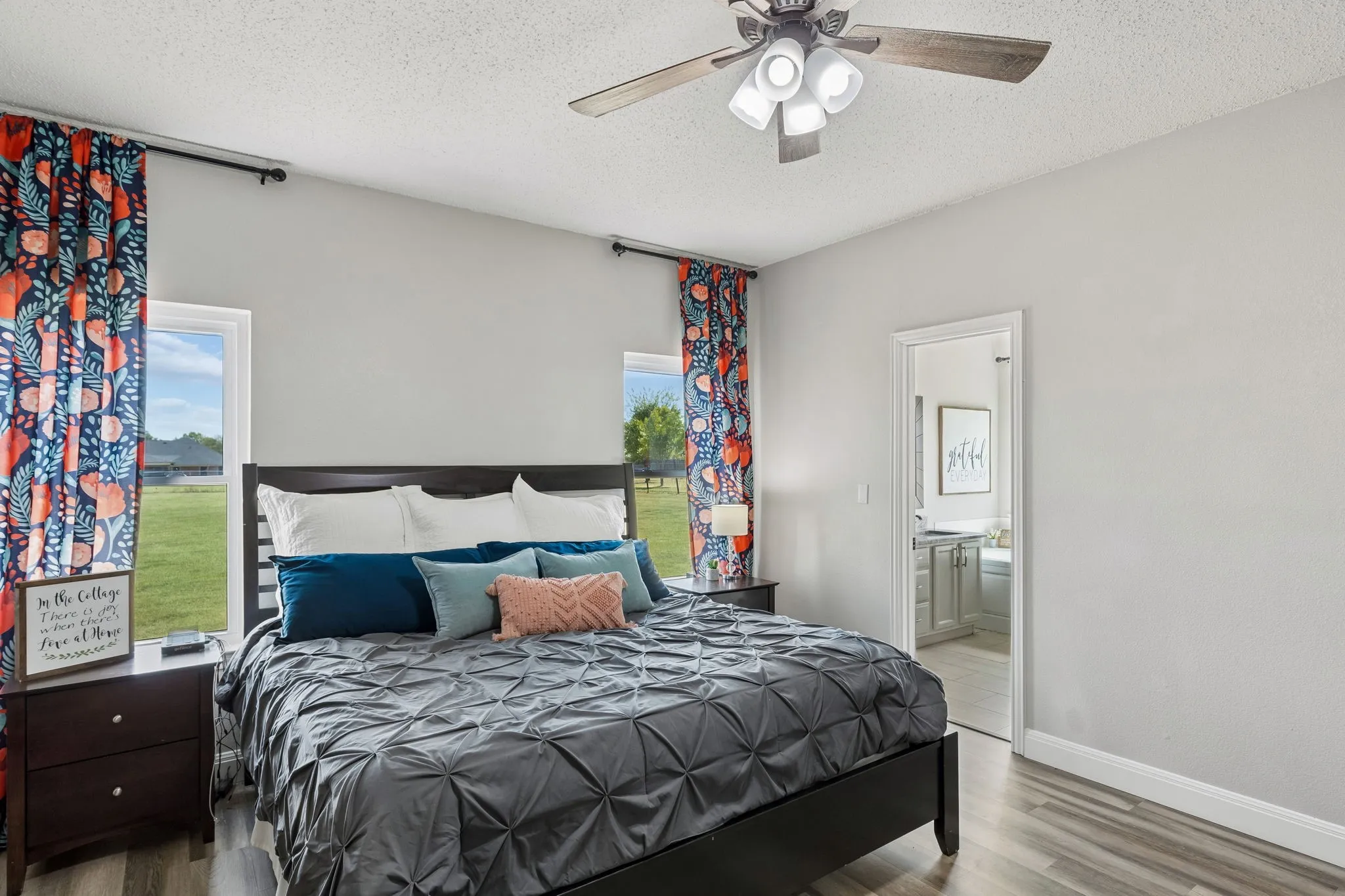 Wood-finish flooring, ceiling fan with integrated lighting, and a doorway leading to an additional space featuring a vanity