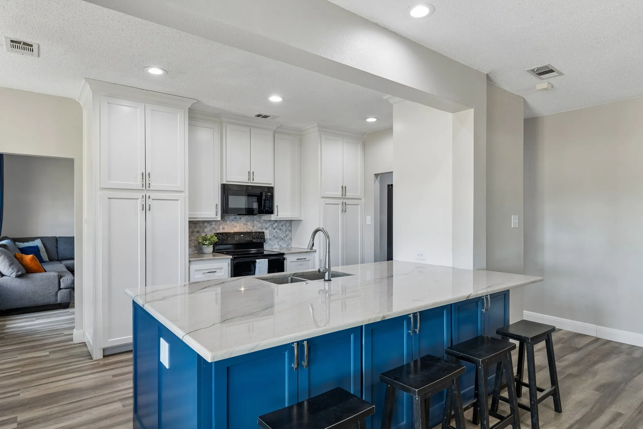 Kitchen featuring white cabinetry, a blue kitchen island with a light-toned countertop, a black range, and wood-finish flooring