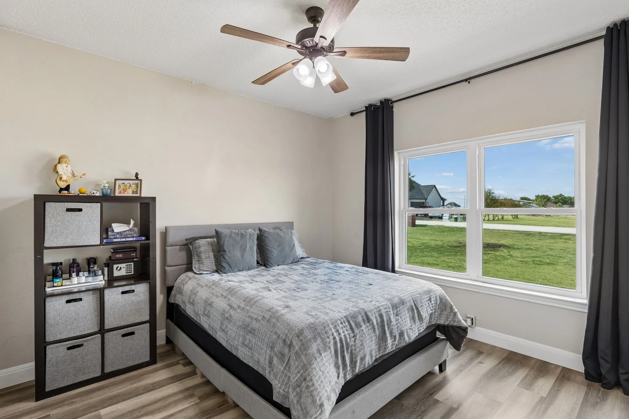 Wood-finish flooring, ceiling fan with integrated lighting, and a large window providing ample natural light