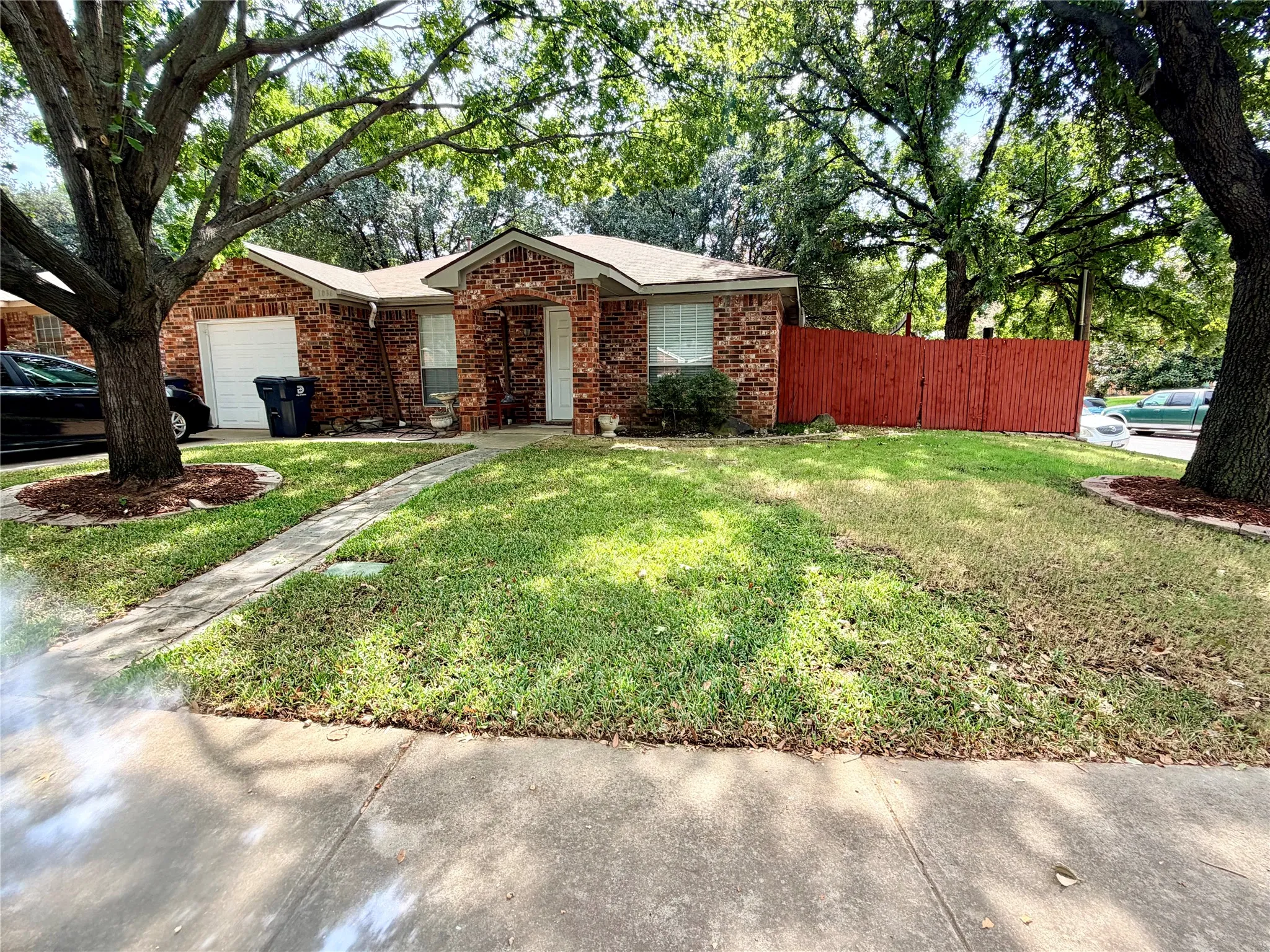 Red brick exterior with white trim, attached garage, concrete walkway, and a red stained wood privacy fence