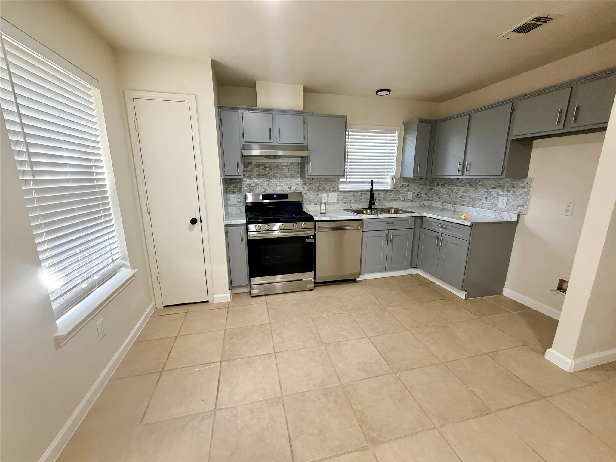Kitchen featuring grey cabinetry, stainless steel appliances, mosaic tile backsplash, light-toned tile flooring, and white countertops