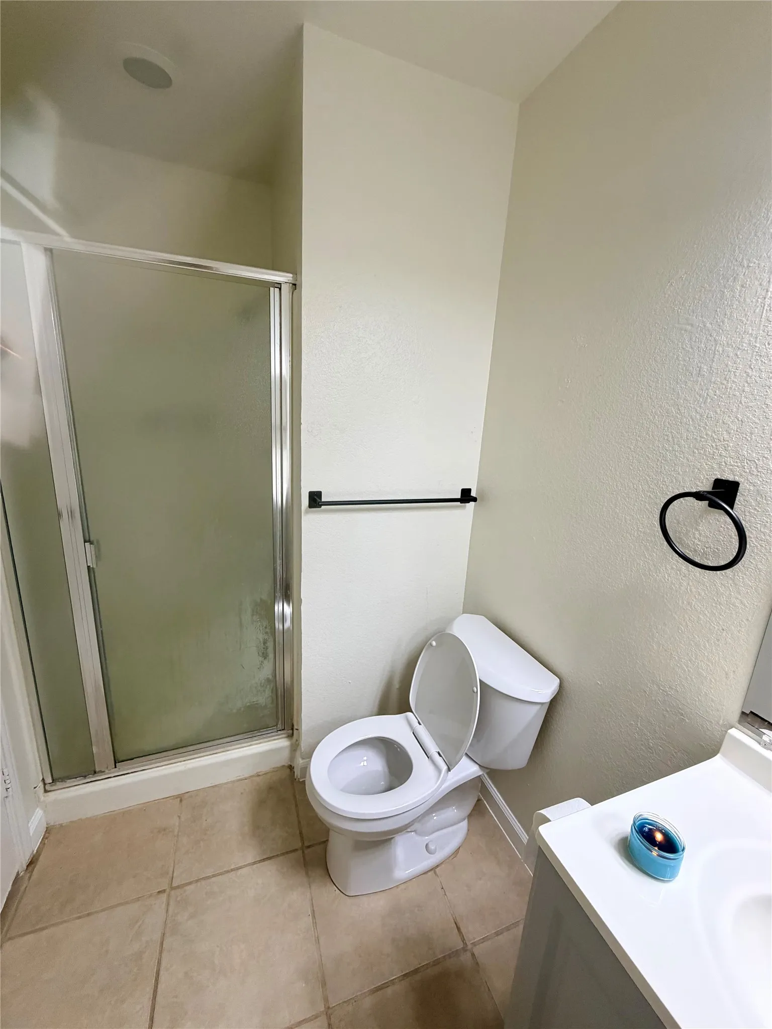 Shower enclosure with frosted glass, tiled flooring, white vanity with integrated sink, and modern black hardware