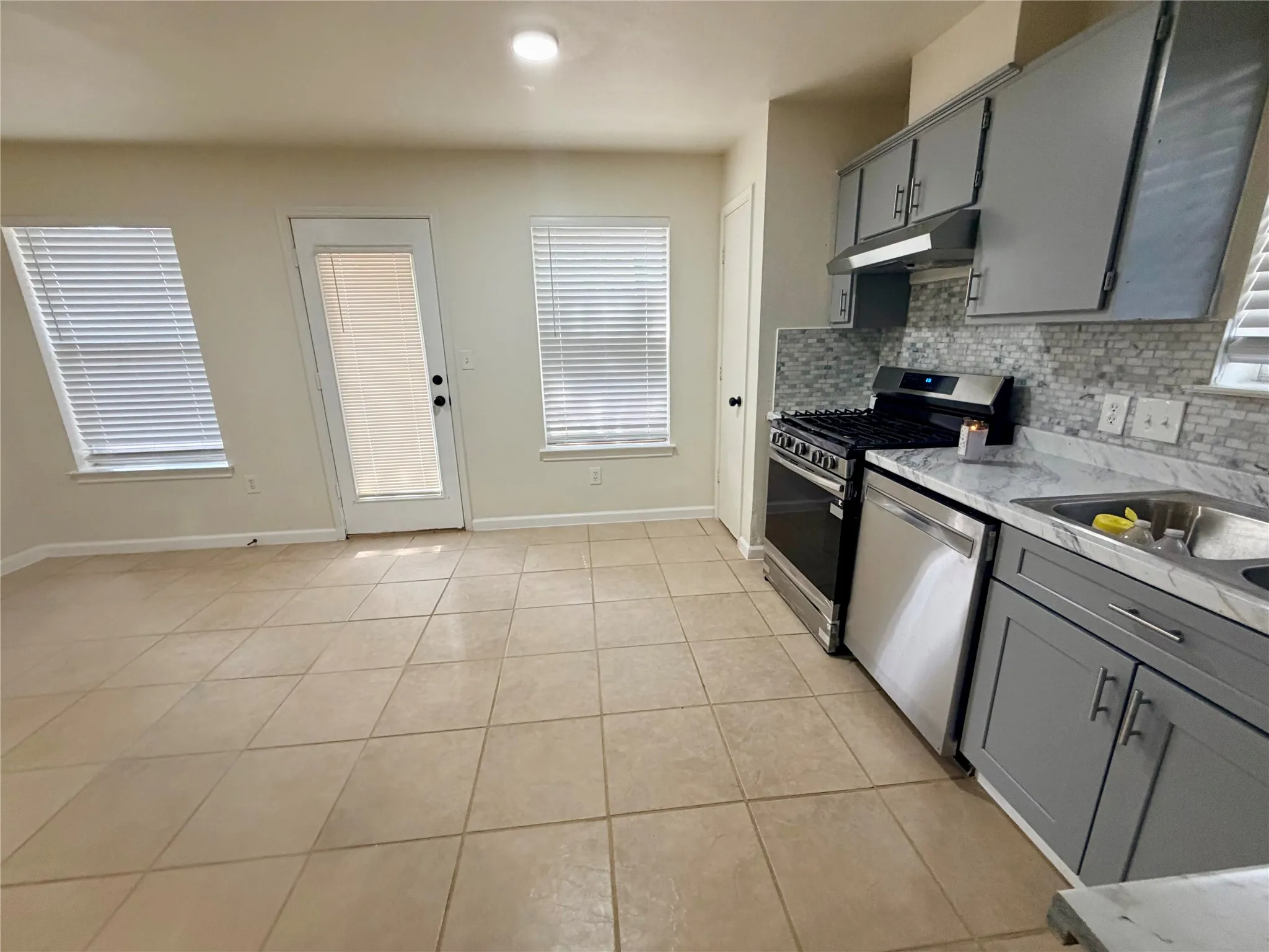 Kitchen with stainless steel appliances, mosaic tile backsplash, gray cabinetry, and light-toned tile flooring