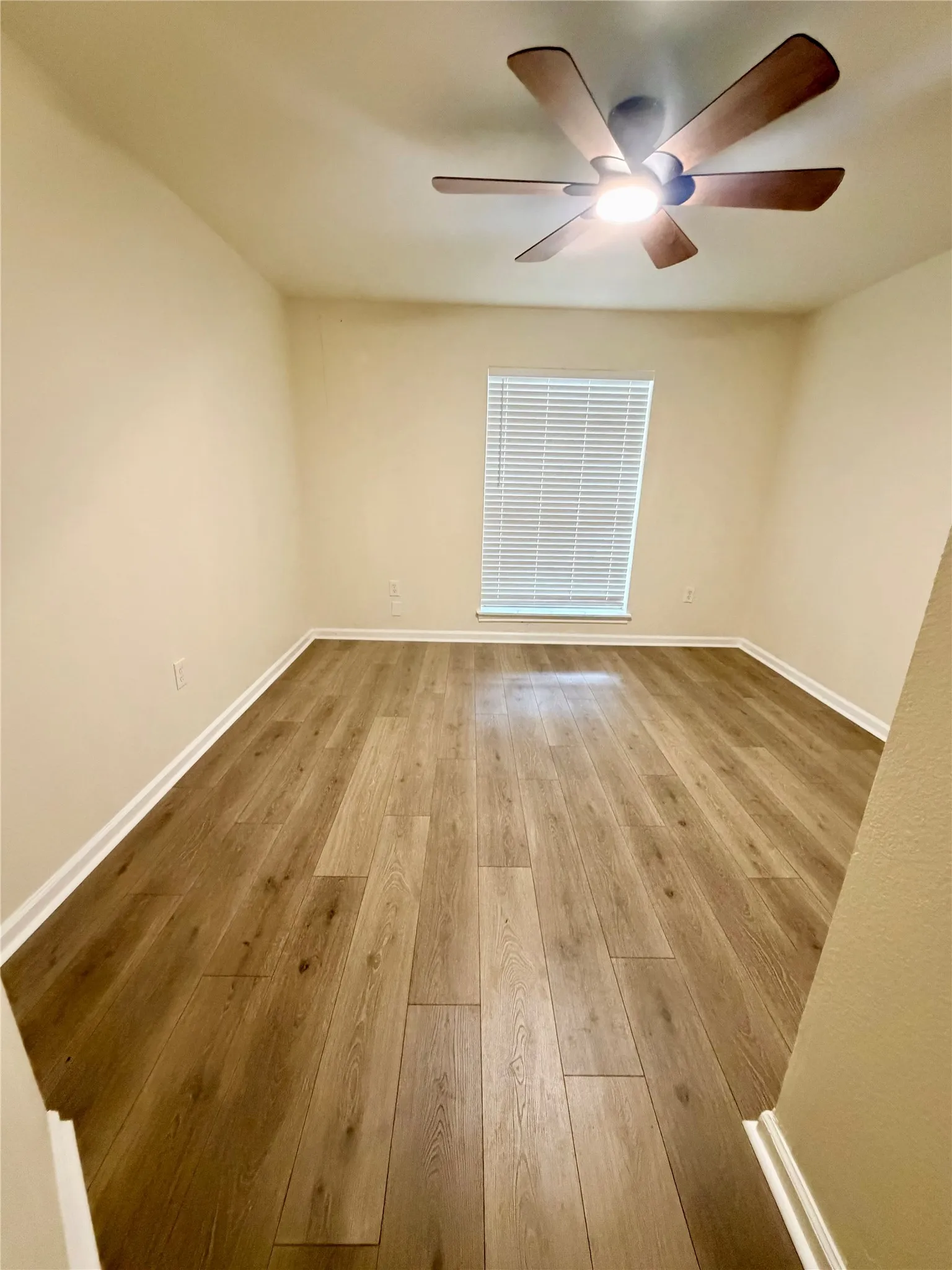 Wood-finish flooring, ceiling fan with integrated lighting, window with blinds, and neutral wall tones