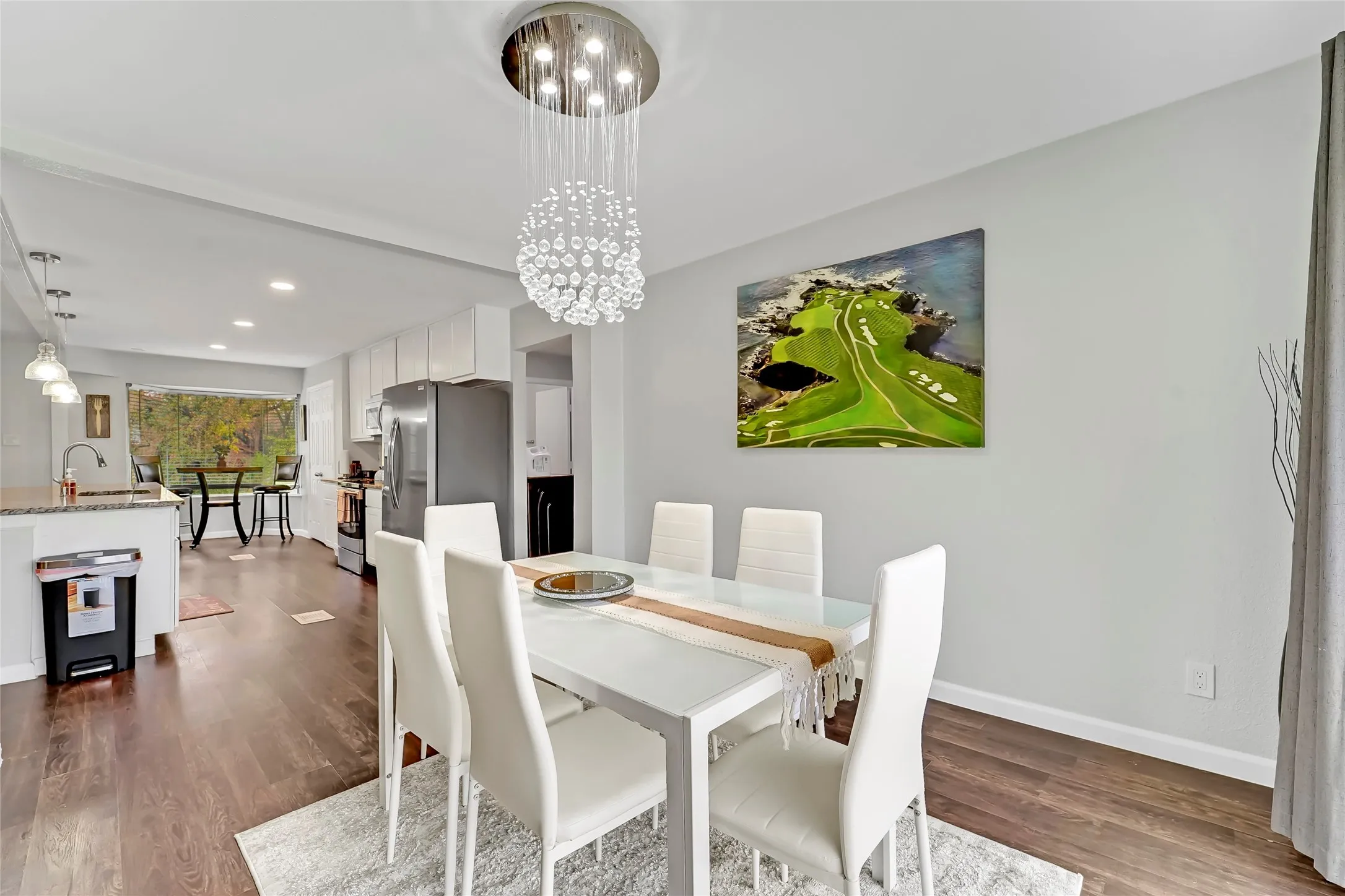 Open-concept dining area with wood-finish flooring, a contemporary chandelier, and a breakfast bar