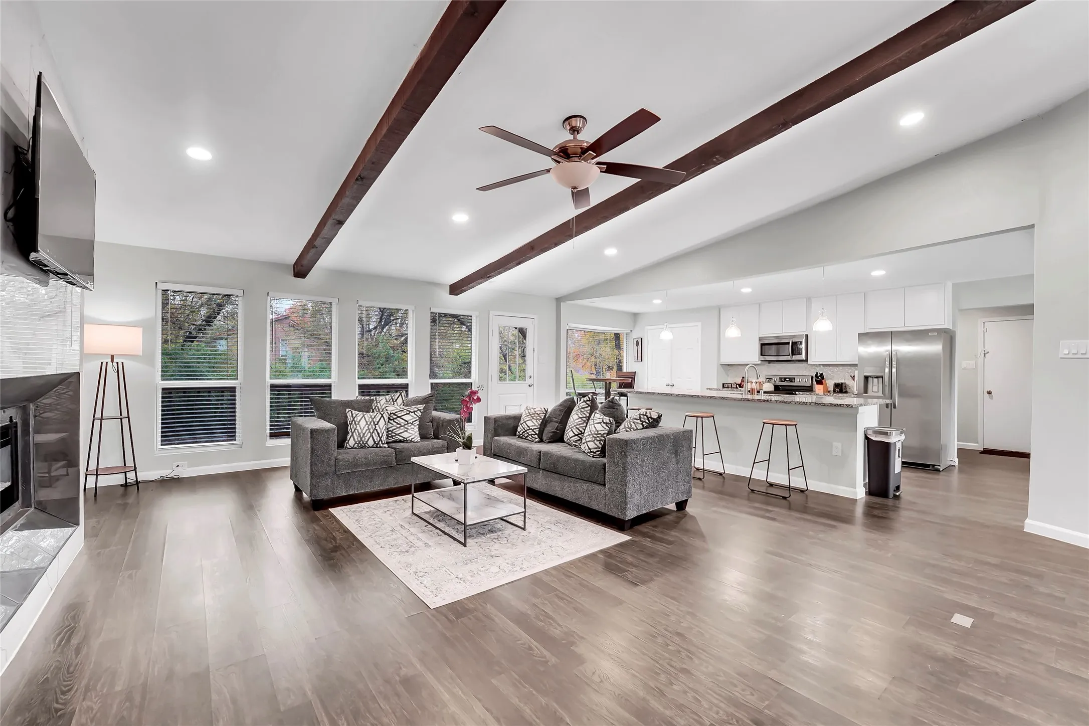Vaulted ceiling with exposed wood beams, recessed lighting, wood-finish flooring, built-in fireplace, and a kitchen island with pendant lighting