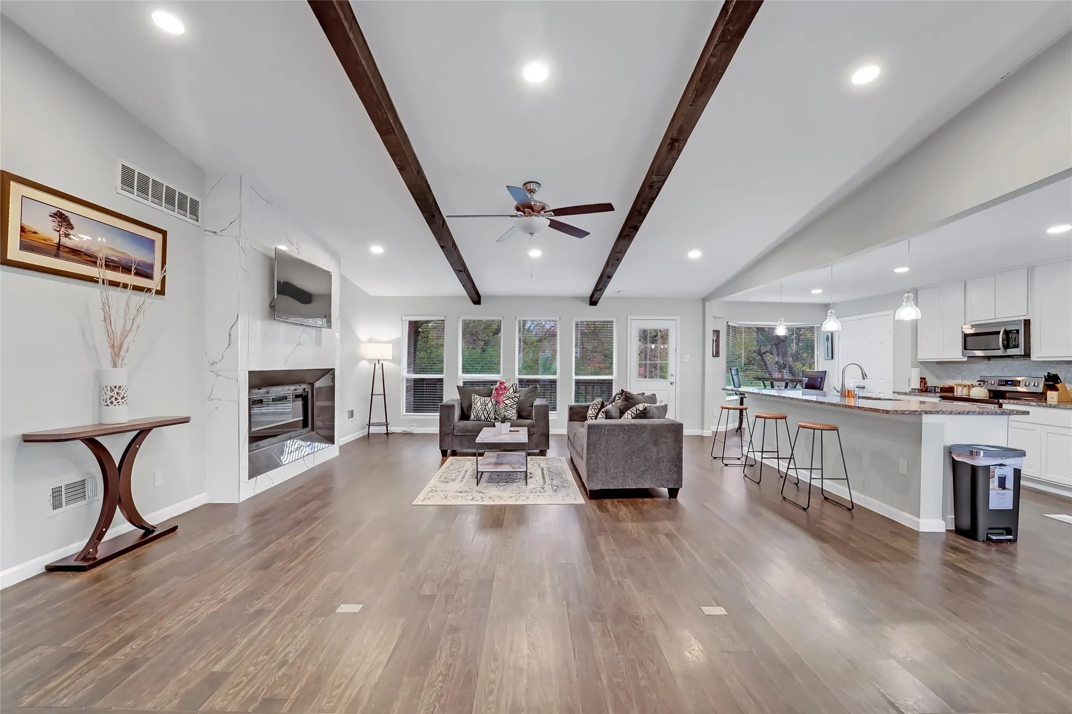 Open-concept living space featuring wood-finish flooring, exposed ceiling beams, a built-in fireplace, and recessed lighting