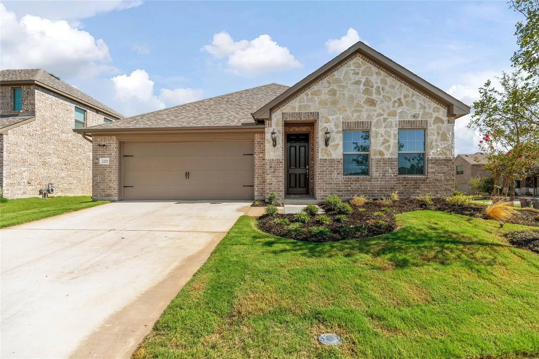 Stone and brick façade with a two-car garage, manicured landscaping, and a covered entryway
