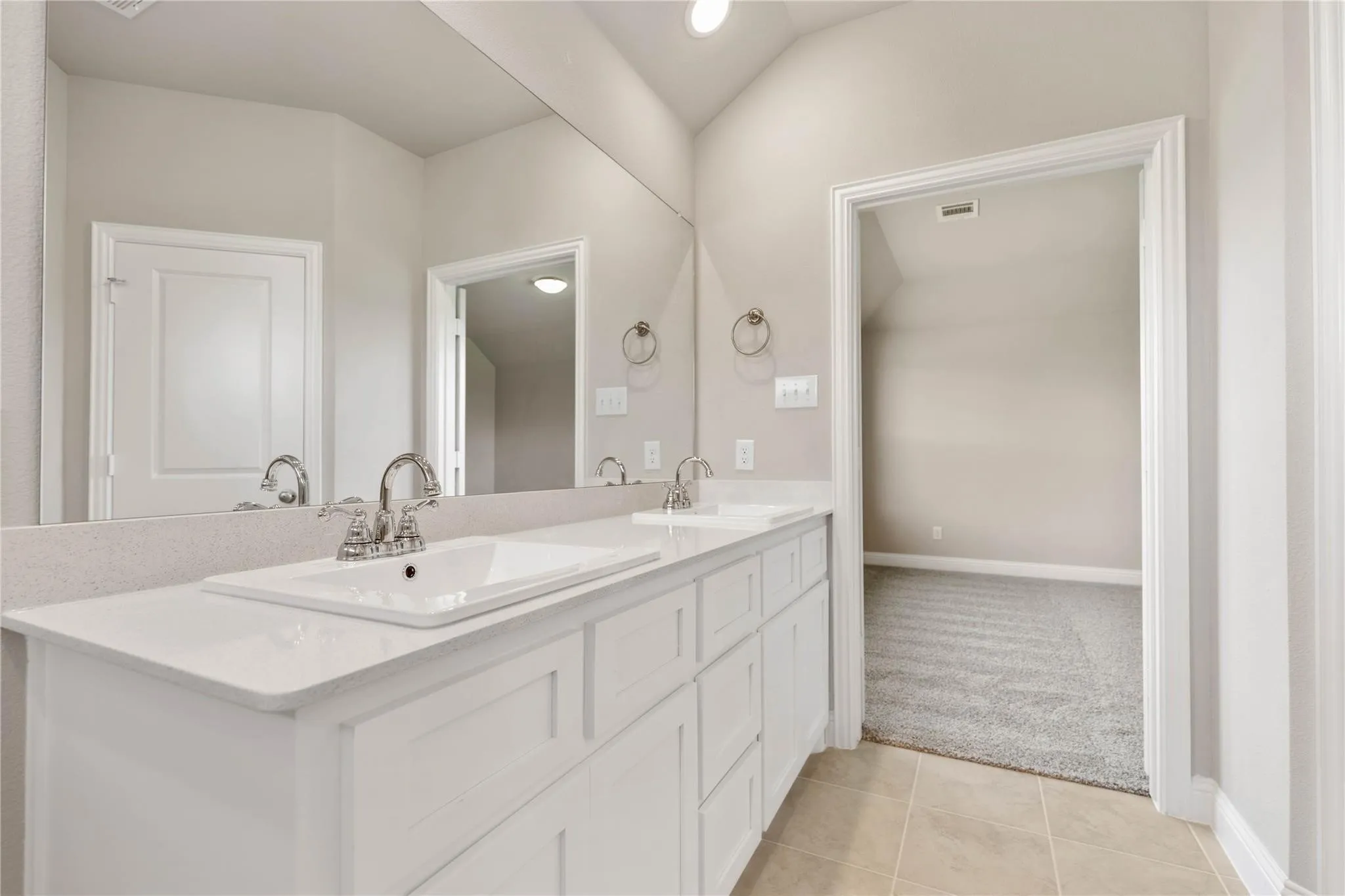 Dual vanity with white cabinetry, integrated sinks, chrome fixtures, and a large wall-mounted mirror
