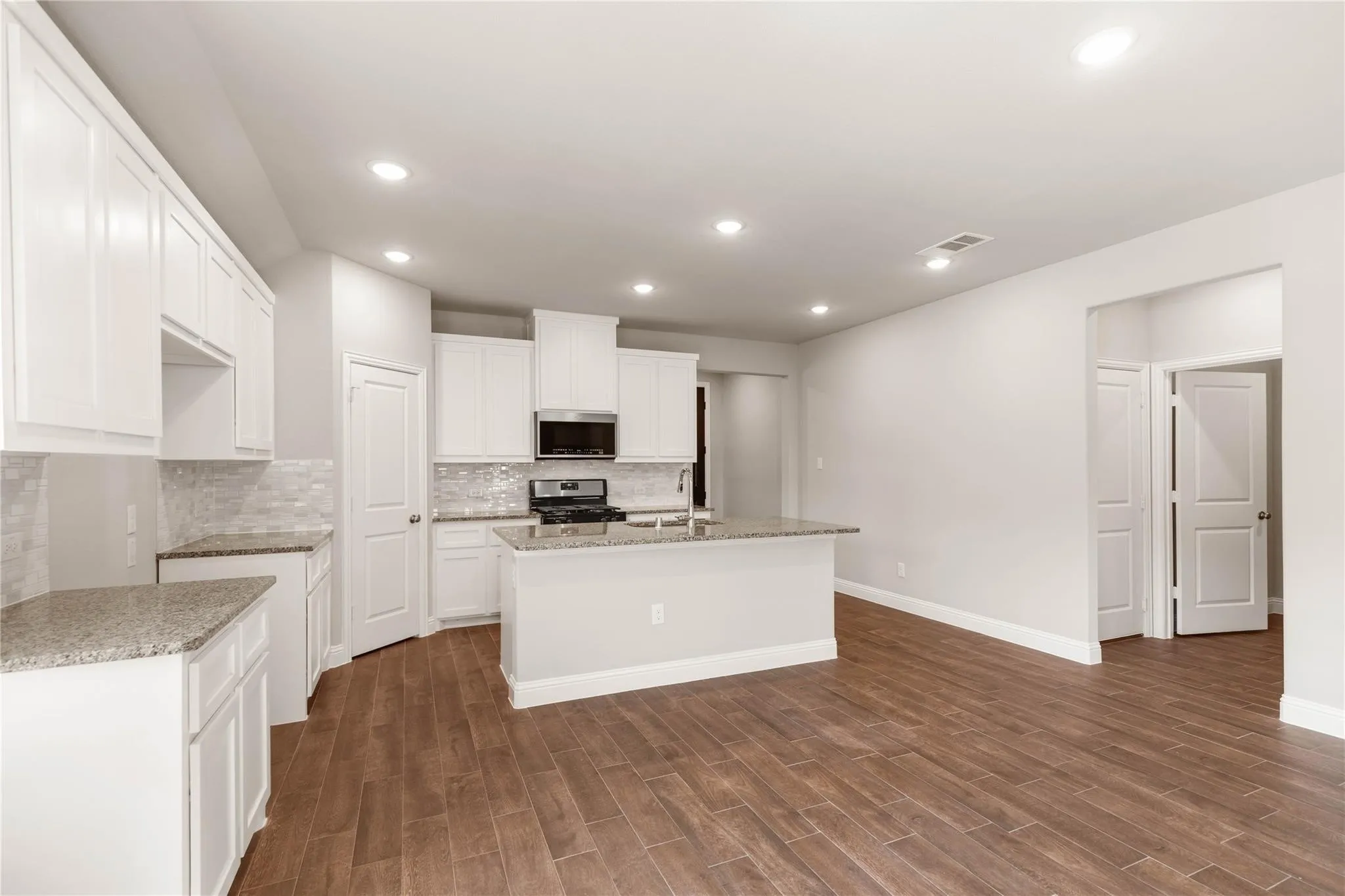 Kitchen featuring white cabinetry, granite countertops, tile backsplash, stainless steel appliances, and wood-finish flooring