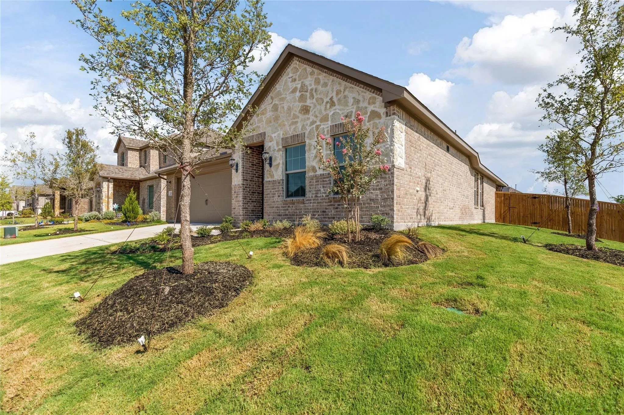 Exterior featuring a combination of brick and stone facade, an attached garage, and a wood privacy fence