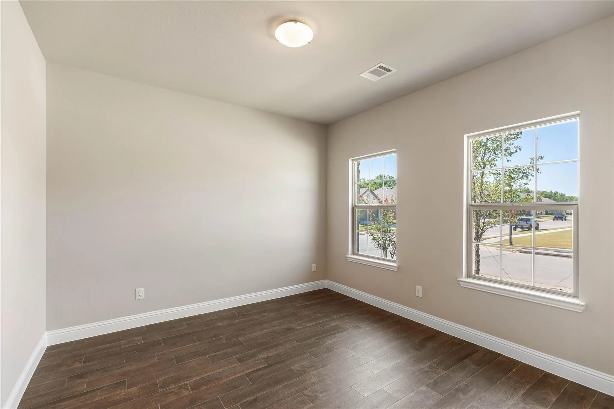 Wood-finish flooring, neutral wall tones, two double-hung windows, and ceiling-mounted lighting