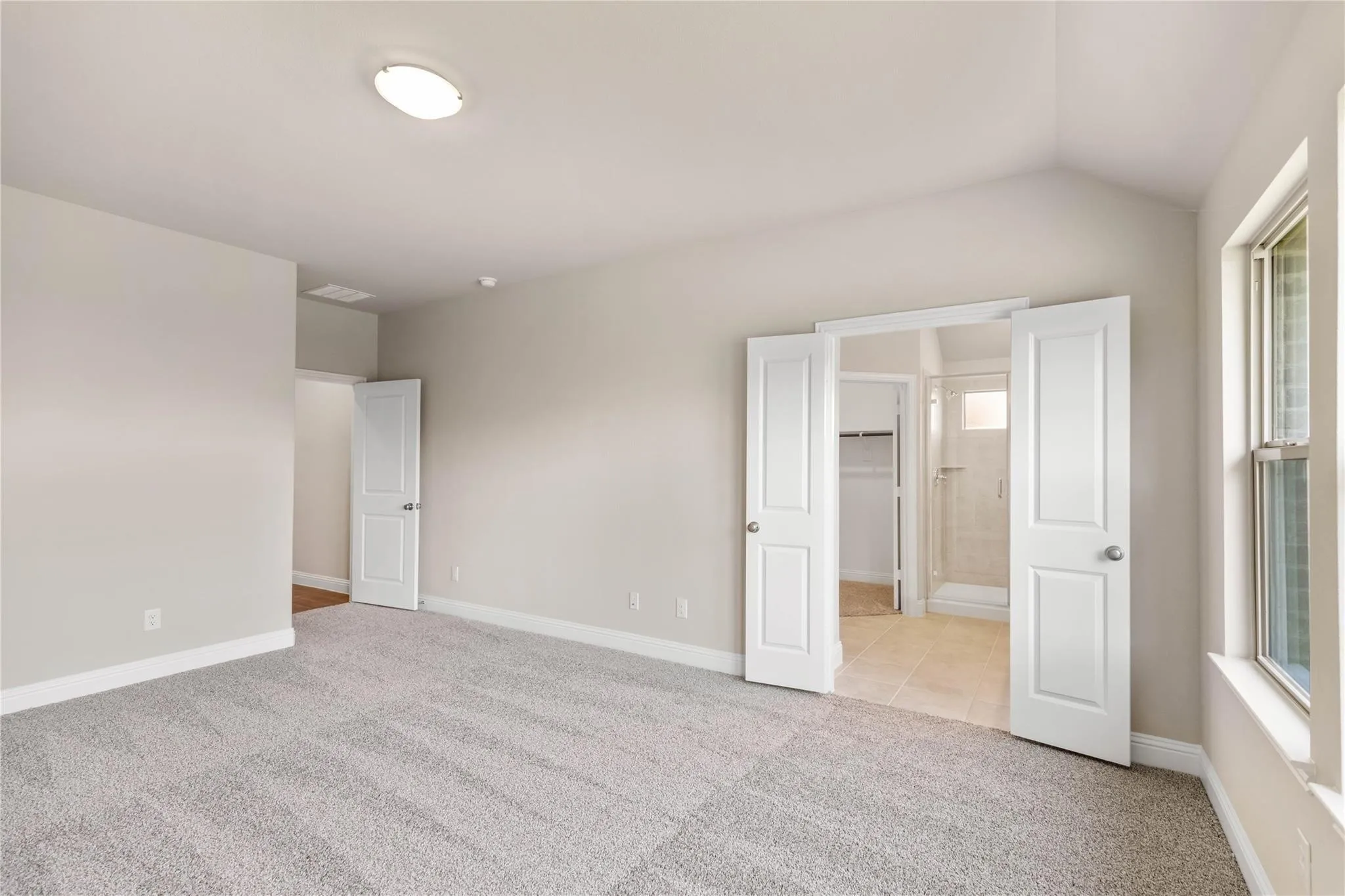 Plush carpeting, vaulted ceiling, double-door entry, tiled bathroom with shower enclosure, and a window for natural illumination