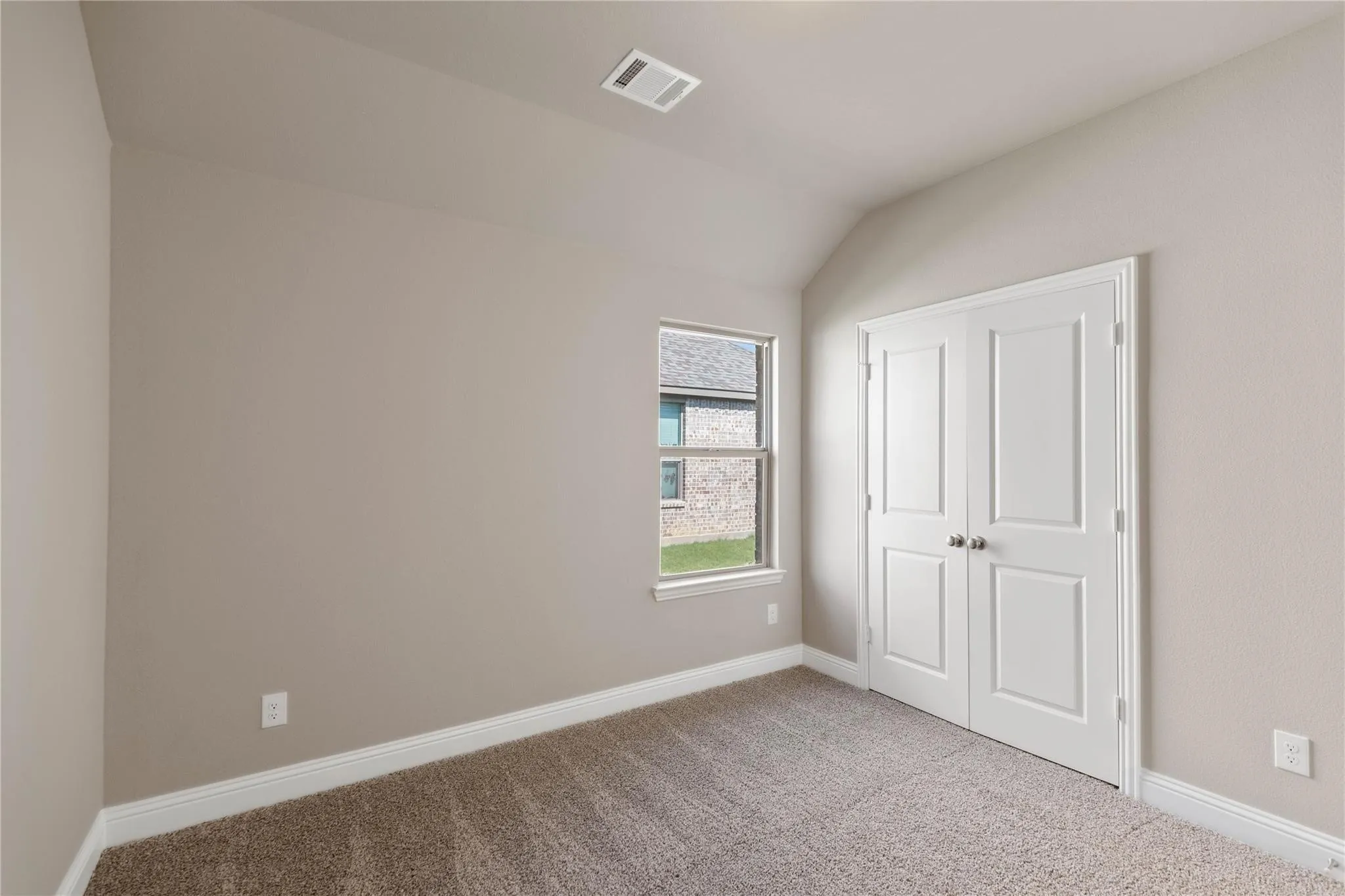 Vaulted ceiling, neutral tone walls, carpeted flooring, window with white trim, and a double-door closet