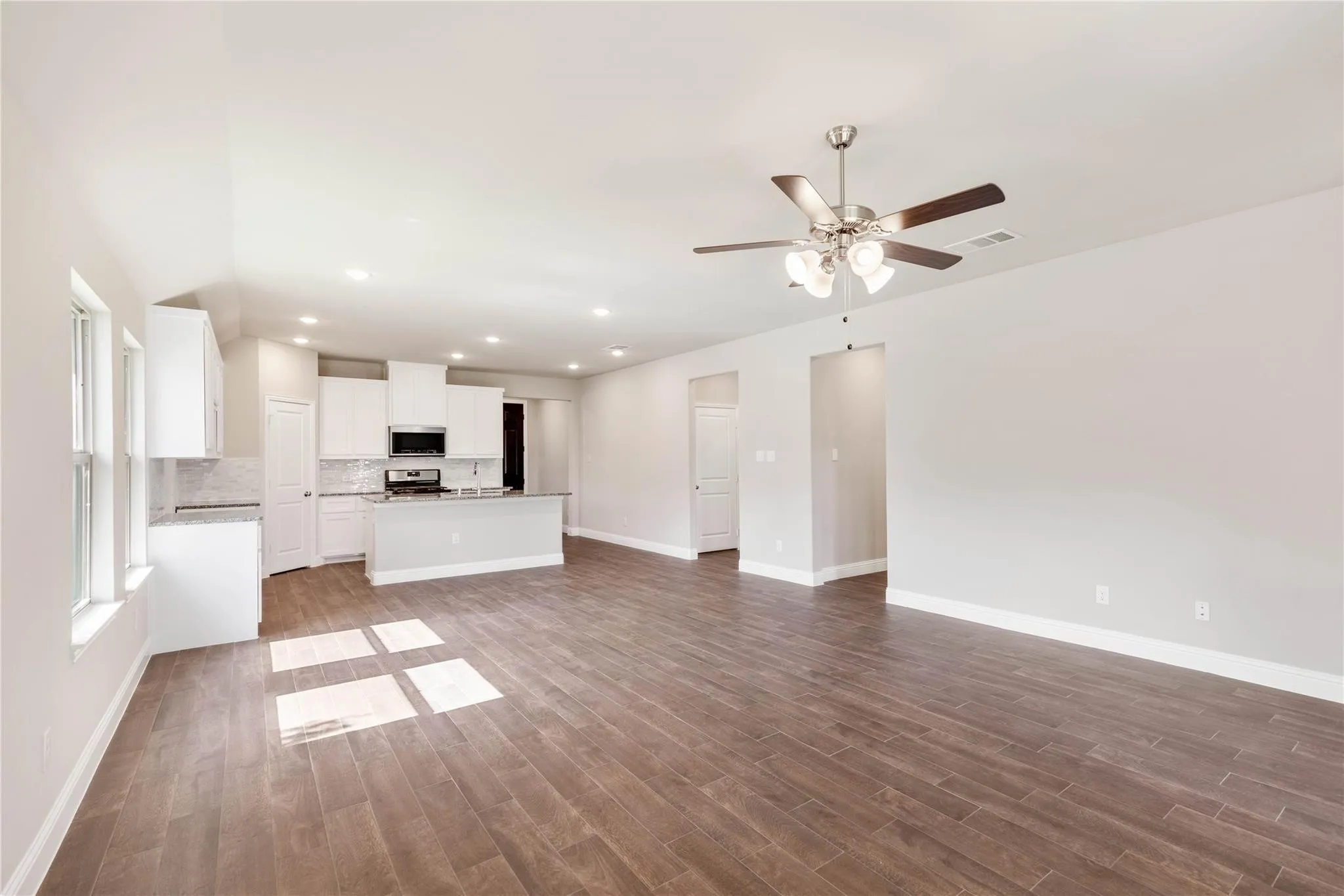 Spacious open-concept layout with wood-finish flooring, white cabinetry, integrated stainless steel appliances, recessed lighting, and a ceiling fan