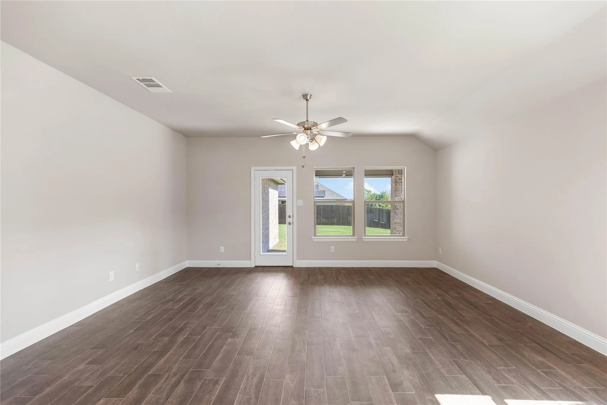 Spacious room featuring wood-finish flooring, vaulted ceiling, ceiling fan, and multiple windows