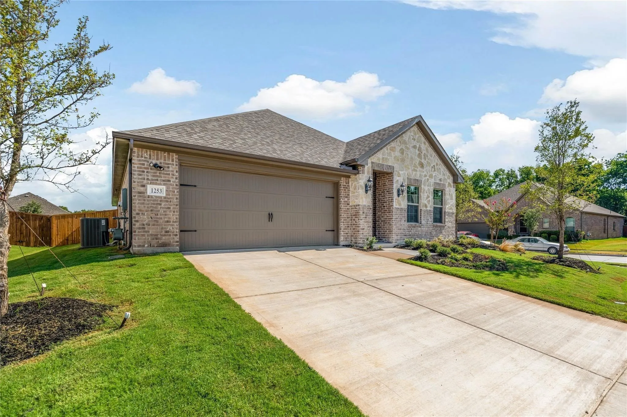 Brick and stone exterior with a concrete driveway, attached two-car garage, and established landscaping