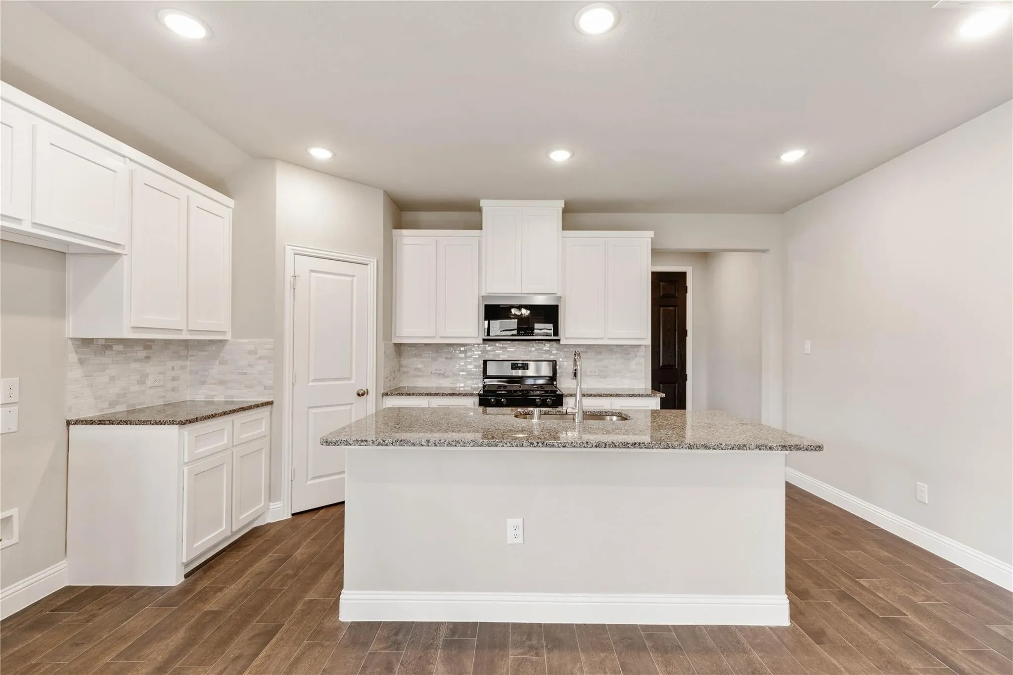 Kitchen featuring white cabinetry, granite countertops, tile backsplash, built-in stainless steel appliances, and wood-finish flooring
