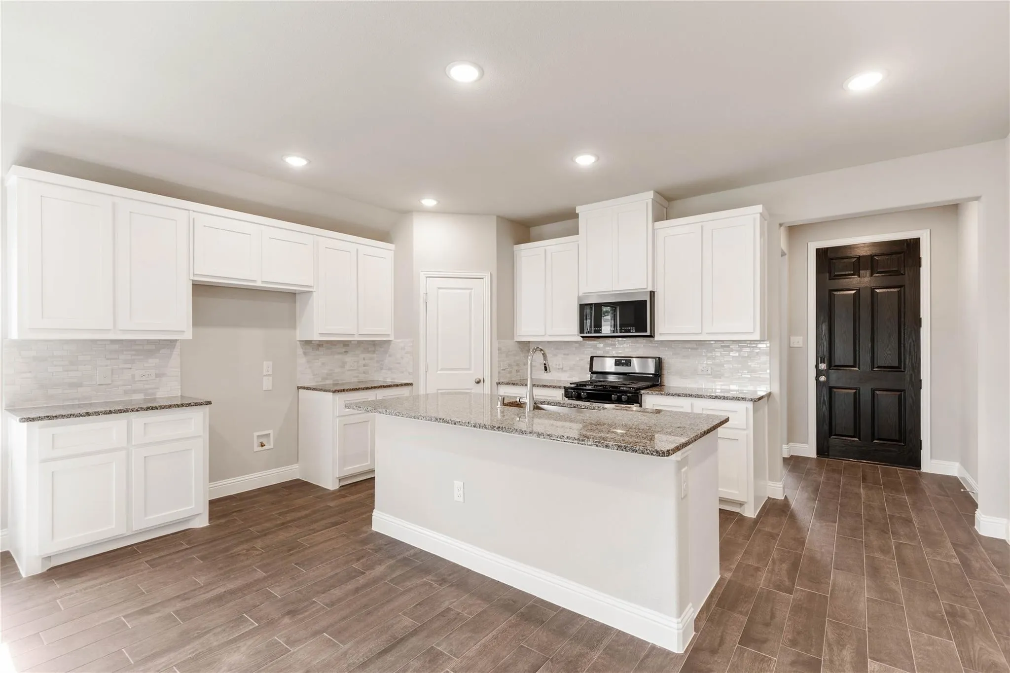Kitchen featuring an island with a sink, white cabinetry, granite countertops, and a tile backsplash