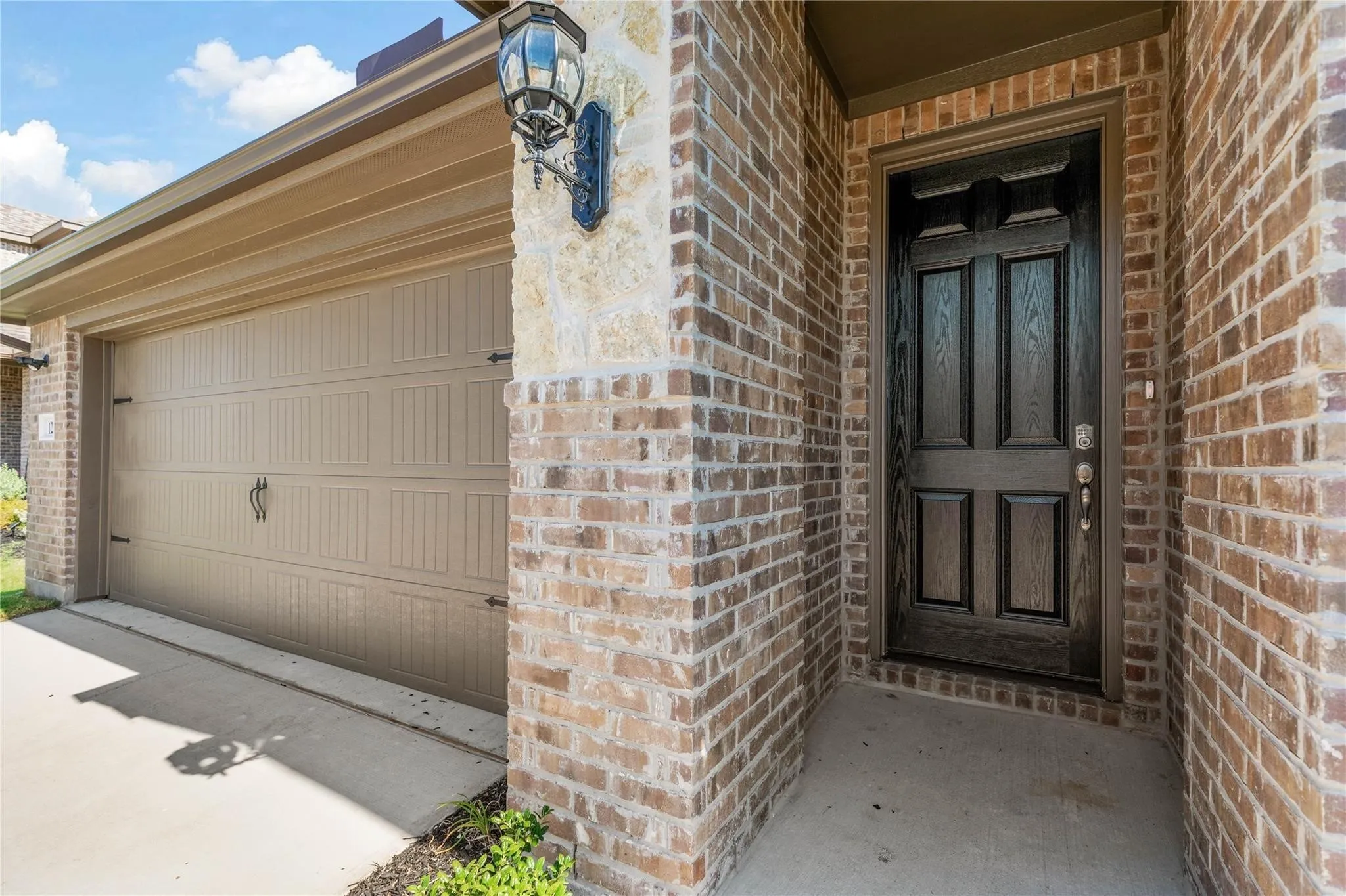 Brick veneer exterior with stone accents, dark wood-finish paneled entry door, and a paneled garage door with decorative hardware