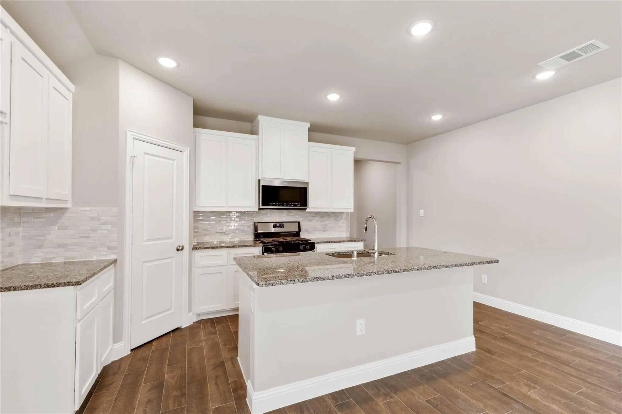 Kitchen featuring white cabinetry, granite countertops, a tile backsplash, recessed lighting, and wood-finish flooring